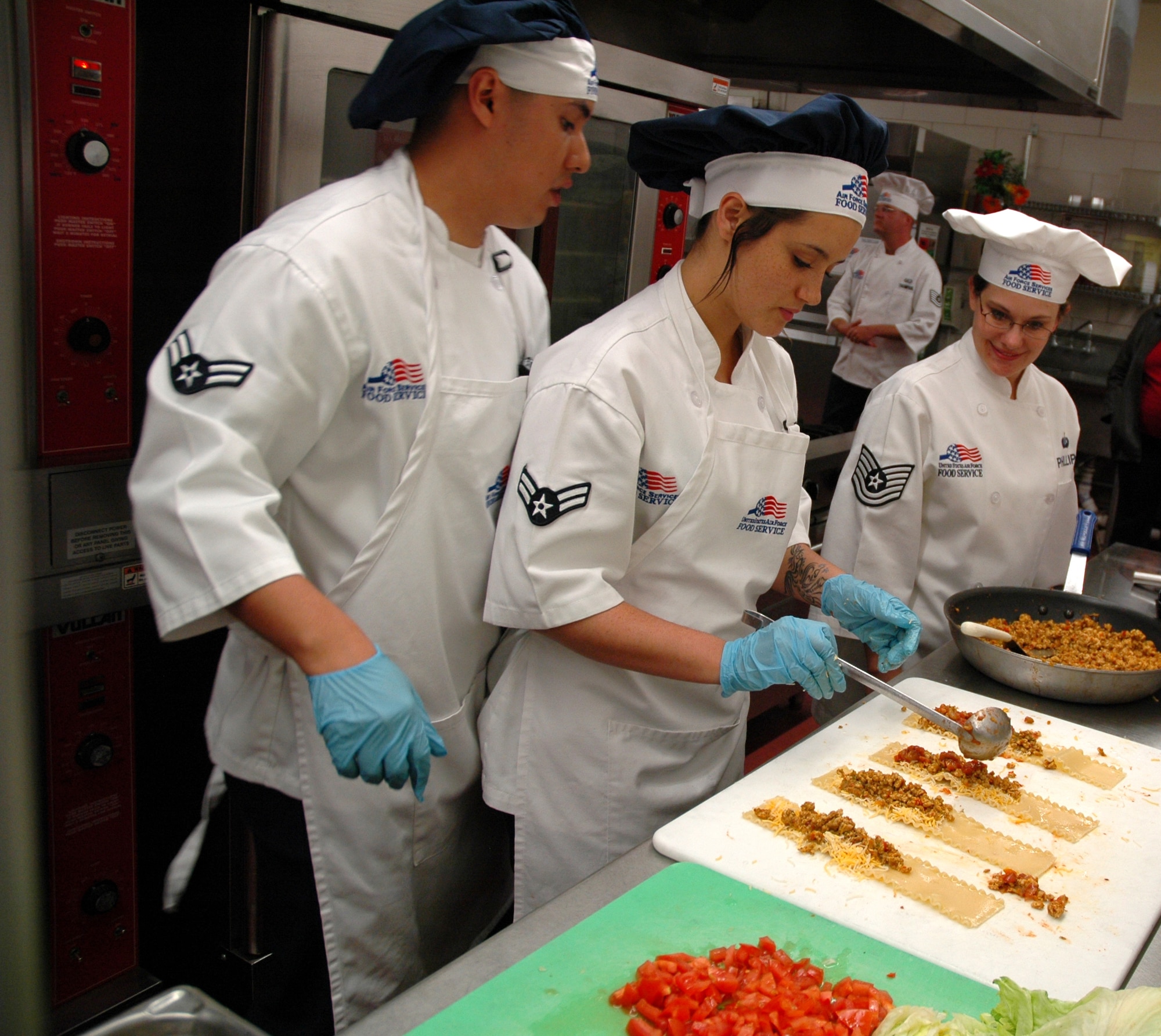 Airmen 1st Class Frank Hernandez and Tanya Cedeno, 341st Force Support Squadron food service specialists, prepare Mexican Chicken Lasagna, while Tech. Sgt. Amy Phillips, 341st Operations Support Squadron NCO in charge of chef training, watches, during a Warrior Chef Competition April 15 at the Elkhorn Dining Facility. (U.S. Air Force photo/Senior Airman Dillon White)