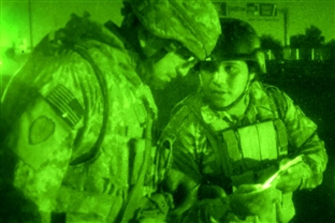 As seen through a night-viewing device, U.S. Army Sgt. Guadalupe Ramos, left, looks at an Iraqi soldier's family photos during a night mission in the Khadra neighborhood of northwest Baghdad, April 20, 2009. During the mission, U.S. and Iraqi soldiers worked together to move barriers from one location to another.
