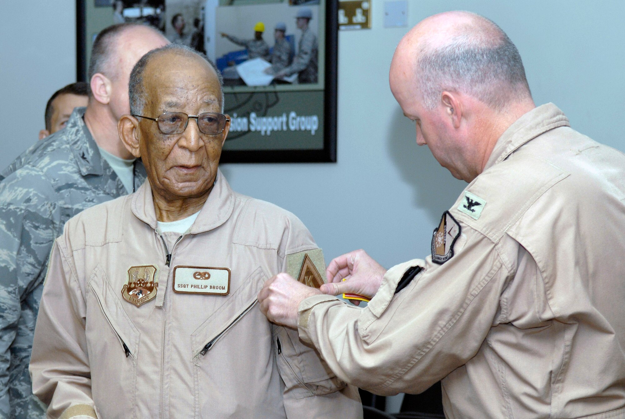 Col. Paul Guemmer, vice commander of the 379th Air Expeditionary Wing, places a wing "triangle K" patch on Tuskegee Airman Phillip Broom April 22 during his visit to the base in Southwest Asia.  The former staff sergeant  served as a jet mechanic during World War II.  The Tuskegee Airmen group shared their stories about  the times they served in the military.  (U.S. Air Force photo/Senior Airman Andrew Satran)    