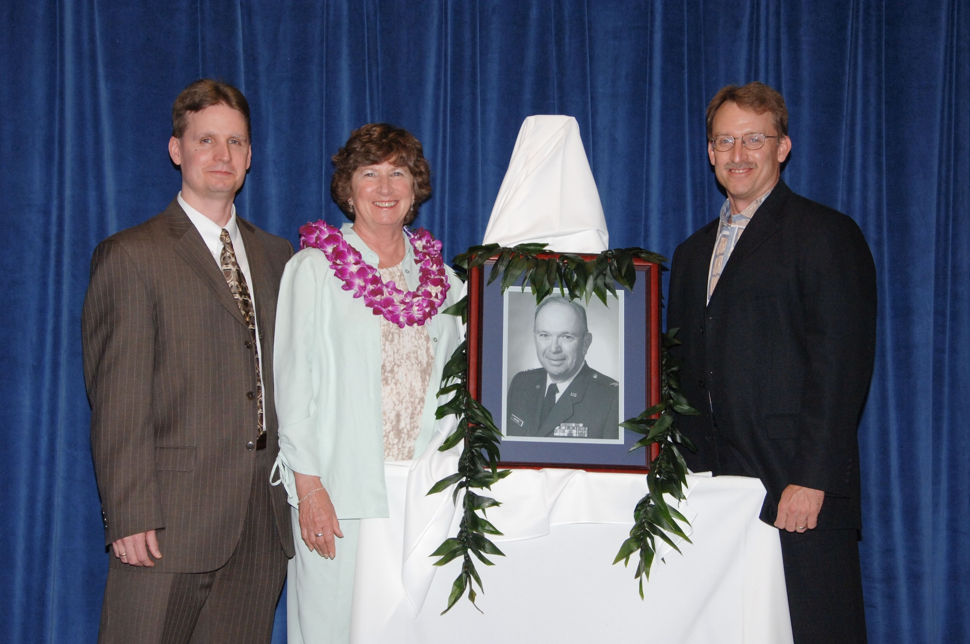 Mrs. Joyce Kaysing stands beside a portrait of her spouse, retired Col. Charles "Chuck" Kaysing, during a ceremony April 17 as the auditorium at the Defense Financial Management and Comptroller School was dedicated in his honor. Colonel Kaysing, who died in 2006, was a former commandant of the school. Also shown are sons Keith and Kevin Kaysing. (U.S. Air Force photo by Melanie Rodgers Cox)