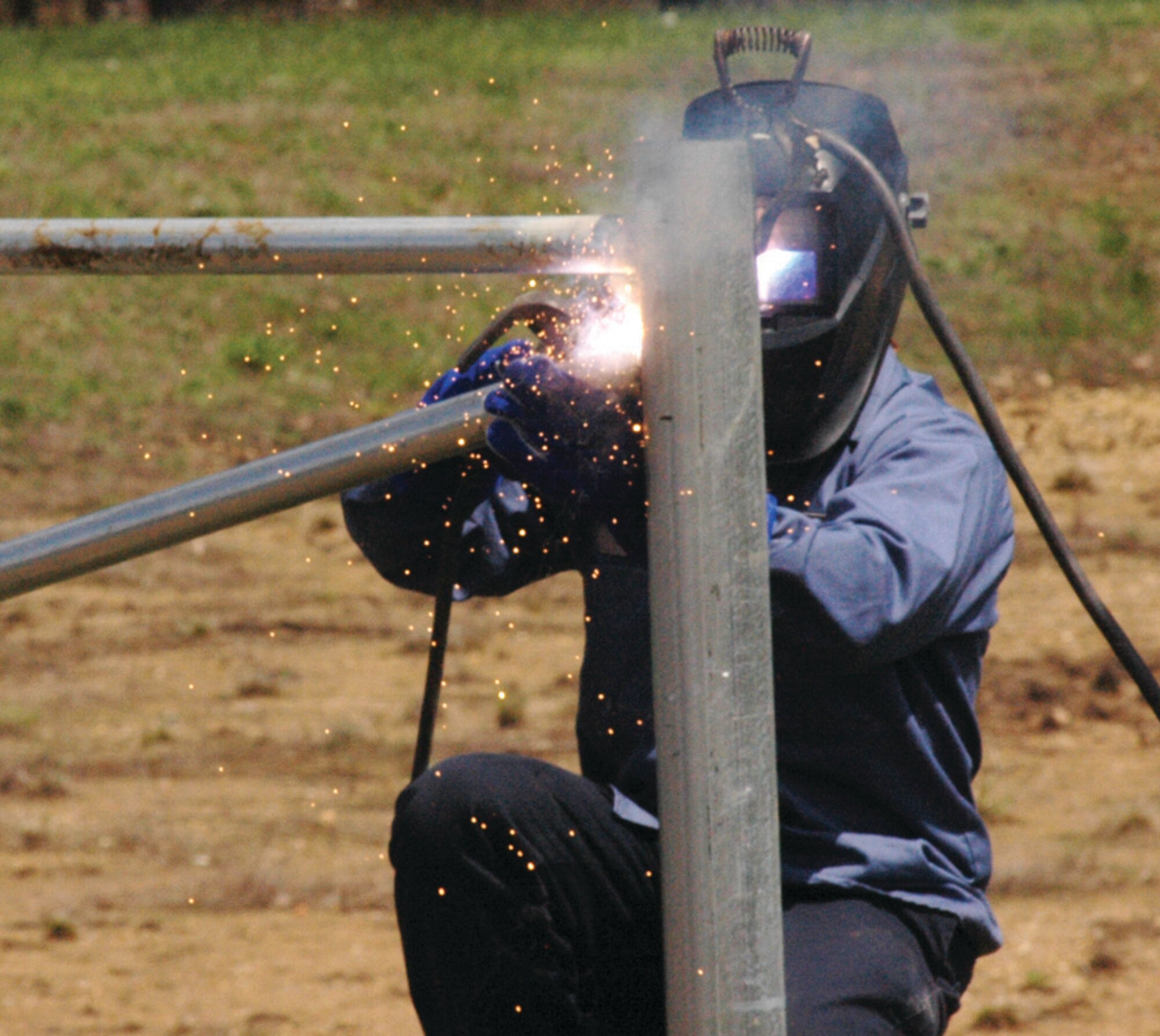 A civilian contractor welds a fence post at the intersection of Alabama Avenue and North Perimeter Road, near the overwatch booth Wednesday. The crash-rated fence will replace  the tombstone barriers, provide more protection and are aesthetically pleasing. (U.S. Air Force photo/ Bobby Jones)