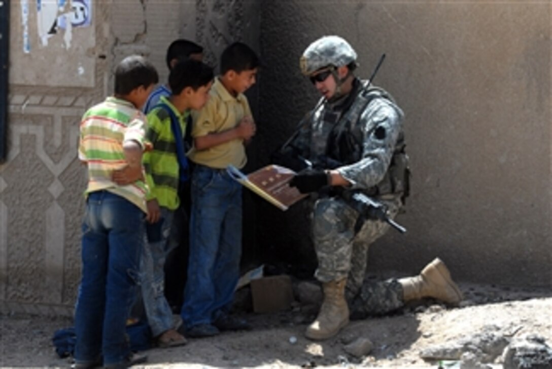 U.S. Army Spc. John Dufrene, attached to the 2nd Brigade, 1st Infantry Division, reads from an English book to Iraqi school children outside the Eserah School in Nassir Wa Salam, Iraq, on April 19, 2009.  The 2nd Brigade, 1st Infantry Division is making sure repairs and structural improvements are being made to schools throughout the Nassir Wa Salam province.  