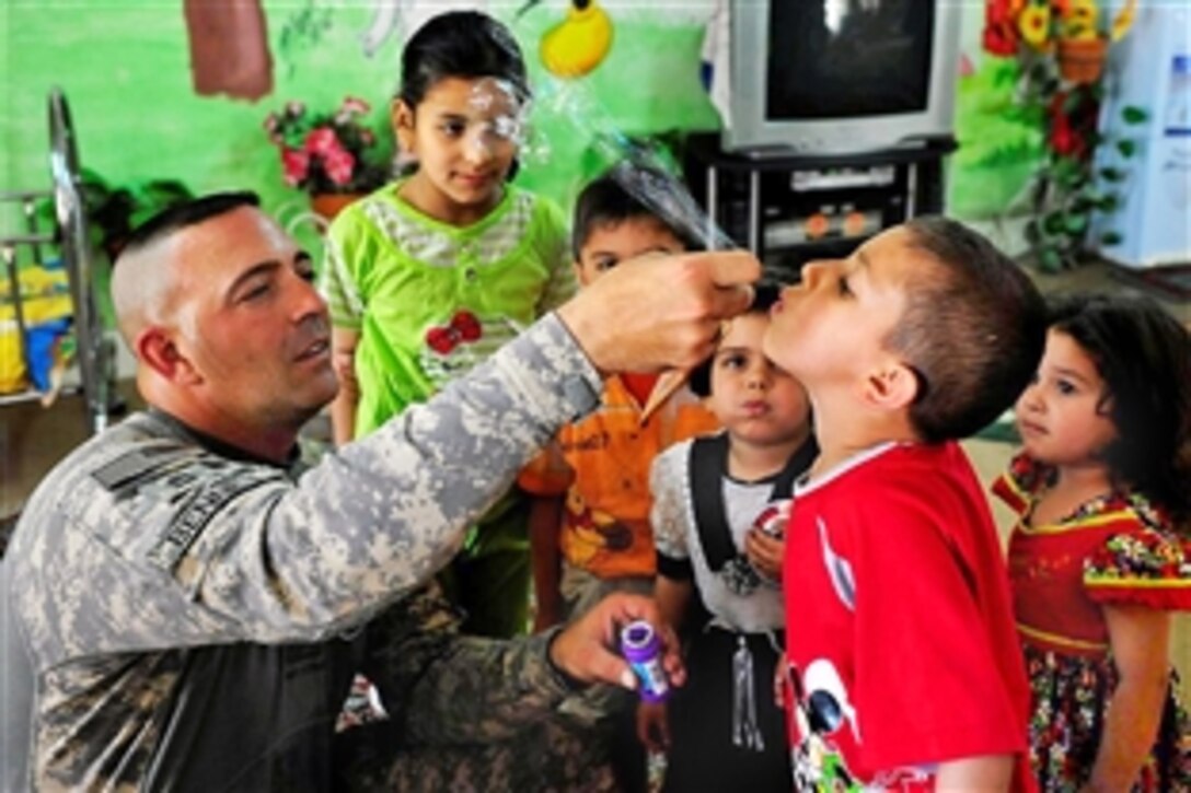 U.S. Army Master Sgt. Mike Bennet helps an Iraqi boy blow bubbles at Al A Alahbab school in Jaeffer, Iraq, April 21, 2009. Bennet is assigned to the 8th Military Police Brigade.