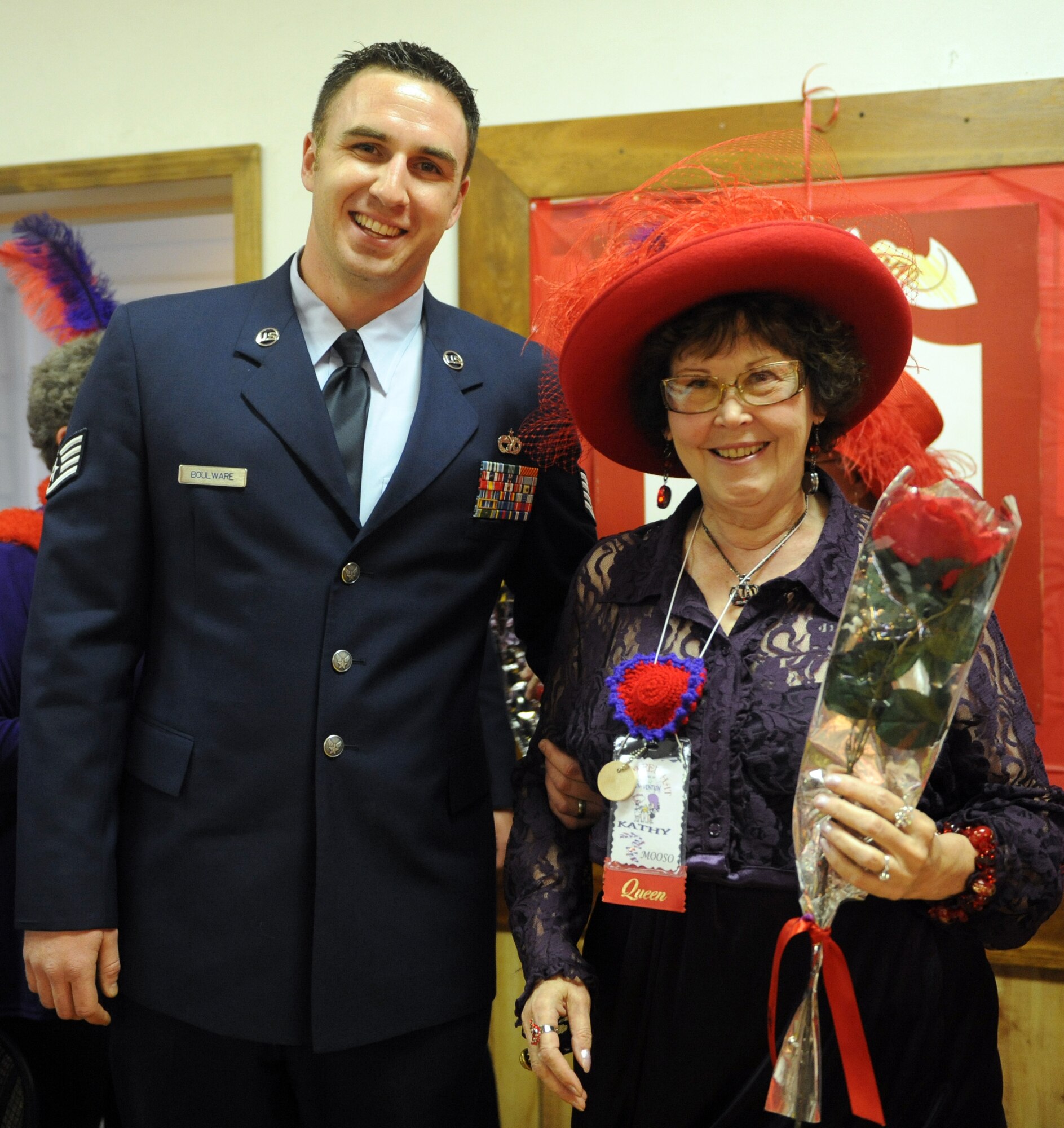 MOUNTAIN HOME AIR FORCE BASE, Idaho -- Staff Sgt. Jimmy Boulware, 366th Logistics Readiness Squadron vehicle operator, escorts Kathy Mooso, a queen in the Red Hat Society, at the American Legion in Mountain Home April 25. Eight drivers from the 366th LRS volunteered to drive more than 157 Red Hat Society members around Elmore County during their annual “funvention” event, which was held in Mountain Home over the weekend. The Red Hat Society is a network of women approaching age 50 and beyond. (U.S. Air Force photo/Airman 1st Class Debbie Lockhart)