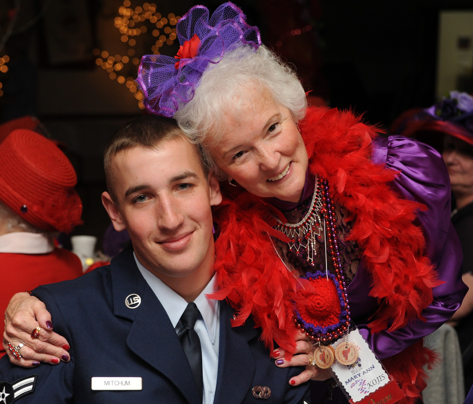 MOUNTAIN HOME AIR FORCE BASE, Idaho -- Airman 1st Class Robert Mitchum, 366th Logistics Readiness Squadron vehicle operator, poses for a picture with Mary Ann Kojes, a queen in the Red Hat Society, at the American Legion in Mountain Home April 25. Eight drivers from the 366th LRS volunteered to drive more than 157 Red Hat Society members around Elmore County during their annual “funvention” event, which was held in Mountain Home over the weekend. The Red Hat Society is a network of women approaching age 50 and beyond. (U.S. Air Force photo/Airman 1st Class Debbie Lockhart)