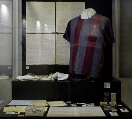 DAYTON, Ohio - In this display is a handmade "ditty bag" made from old undershirts, two needles and thread that a POW made from electrical wire by grinding them to proper size and shape on concrete and sharpening a nail to a point and using it as a punch for the eyes, a shirt issued prior to mid-1968 with the embroidery done in August 1972 by Capt. Edward Mechenbier of Dayton from a photo of his wife (he made his needles and thread from copper wire and an old blanket), metal repair tongs made by a POW for pulling straps through sandals, a skull cap made of two socks sent from home, undershorts mailed to a POW by his wife, who embroidered the hearts, in November 1969, a rosary made from bread colored with ink and string taken from a cotton blanket, pencil made of bread and cloth rolled over a toothpaste tube  with the lead was made of charcoal and soap, playing cards used by Capt. Tom Moe to play solitaire and bridge, dice made of bread dough, ashes and toothpaste, a North Vietnamese pen, a ring made from a toothbrush handle, a pinball game received in a parcel from home, the "Acey Deucy" game pieces made of bread, ashes, and Kool-Aid received in a parcel from home, parts of Shakespeare’s plays printed by a POW on toilet paper, poetry on cigarette wrappers, a book made in Hoa Lo for language classes and cigarette cases. These artifacts are part of the Return with Honor: American Prisoners of War in Southeast Asia exhibit in the Southeast Asia War Gallery at the National Museum of the U.S. Air Force. (U.S. Air Force photo)