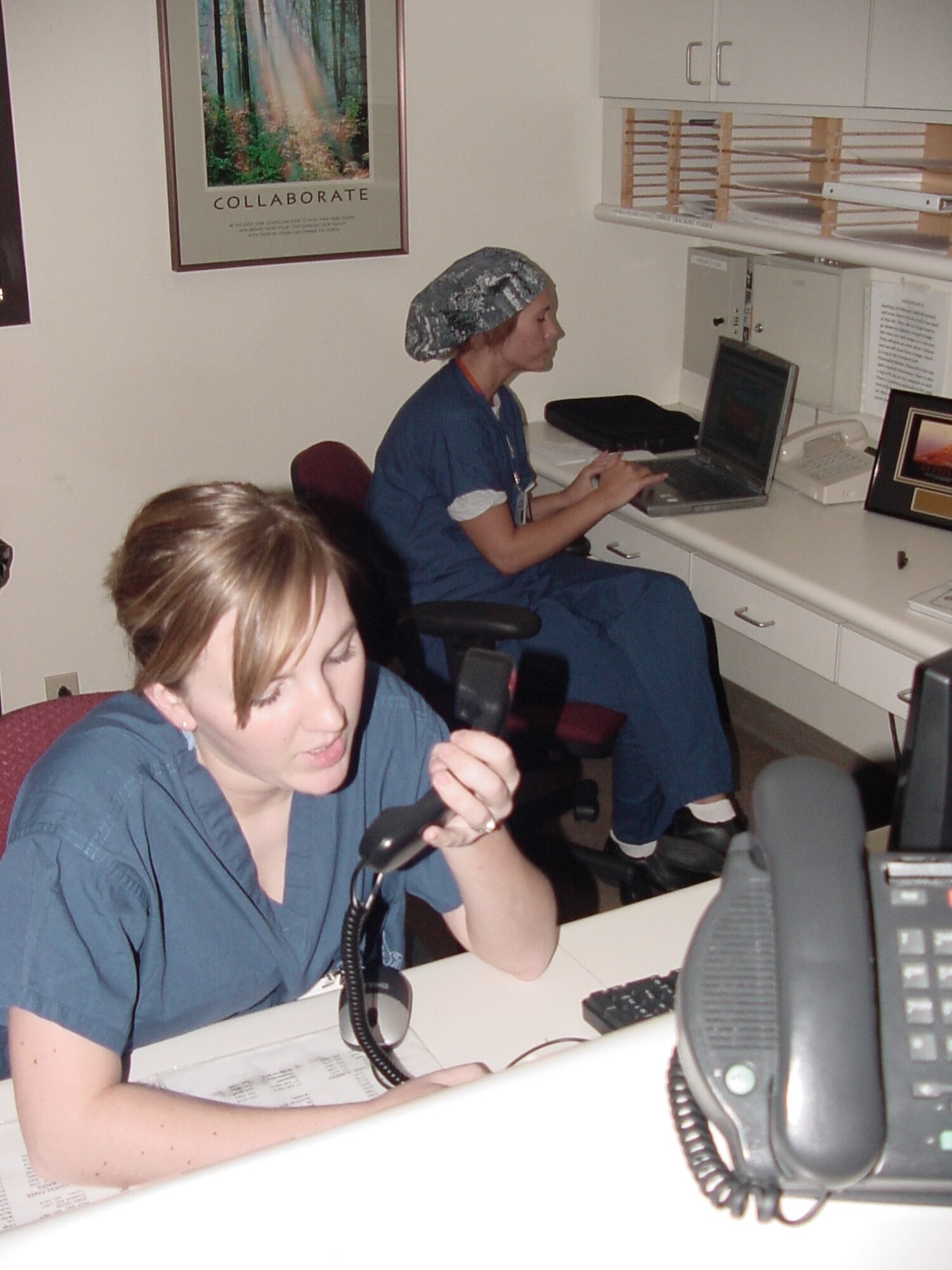 Airman 1st Class Caitlin Bunten, (foreground), a surgical technician with the 60th Surgical Operations Squadron, makes an overhead page while fellow 60th MSGS technician Senior Airman Lisa Maskey types up a report in the Surgical Ward reception station at David Grant USAF Medical Center. (USAF Photo / Jim Spellman)