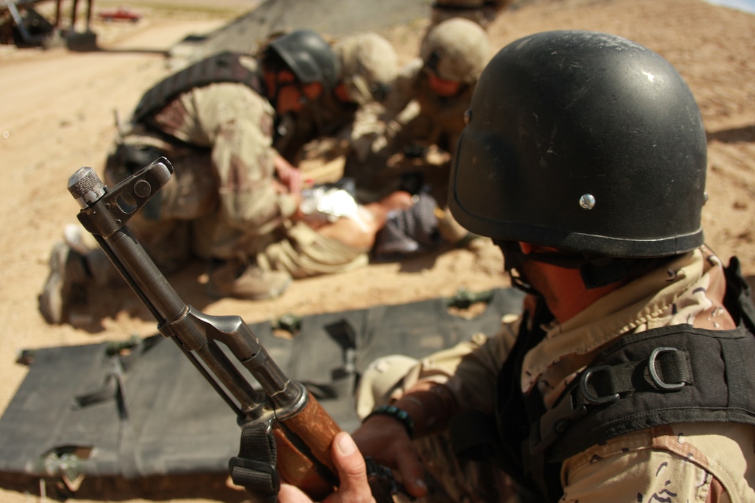 An Iraqi role player with the Advisor Training Group watches as other role players, along with Marines and sailors, patch up fake casualties after a blast from a mock improvised explosive device May 1 at the Combat Center’s Gypsum Ridge training area.