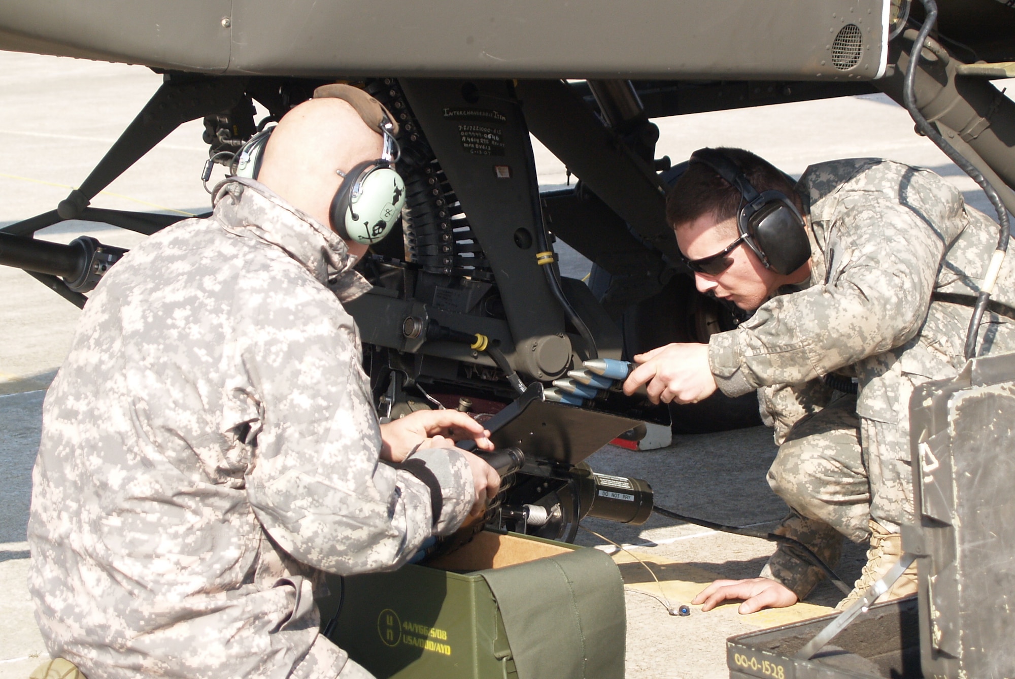Staff Sgt. Benjamin Berislavich, of Knob Noster, prepares to hand Private First Class Jeremy Harshner, of Lone Jack, some 30-mm bullets to continue to load into the chain gun located on the bottom of the Apache gunship. (Photo by Rachel Knight/Missouri National Guard)