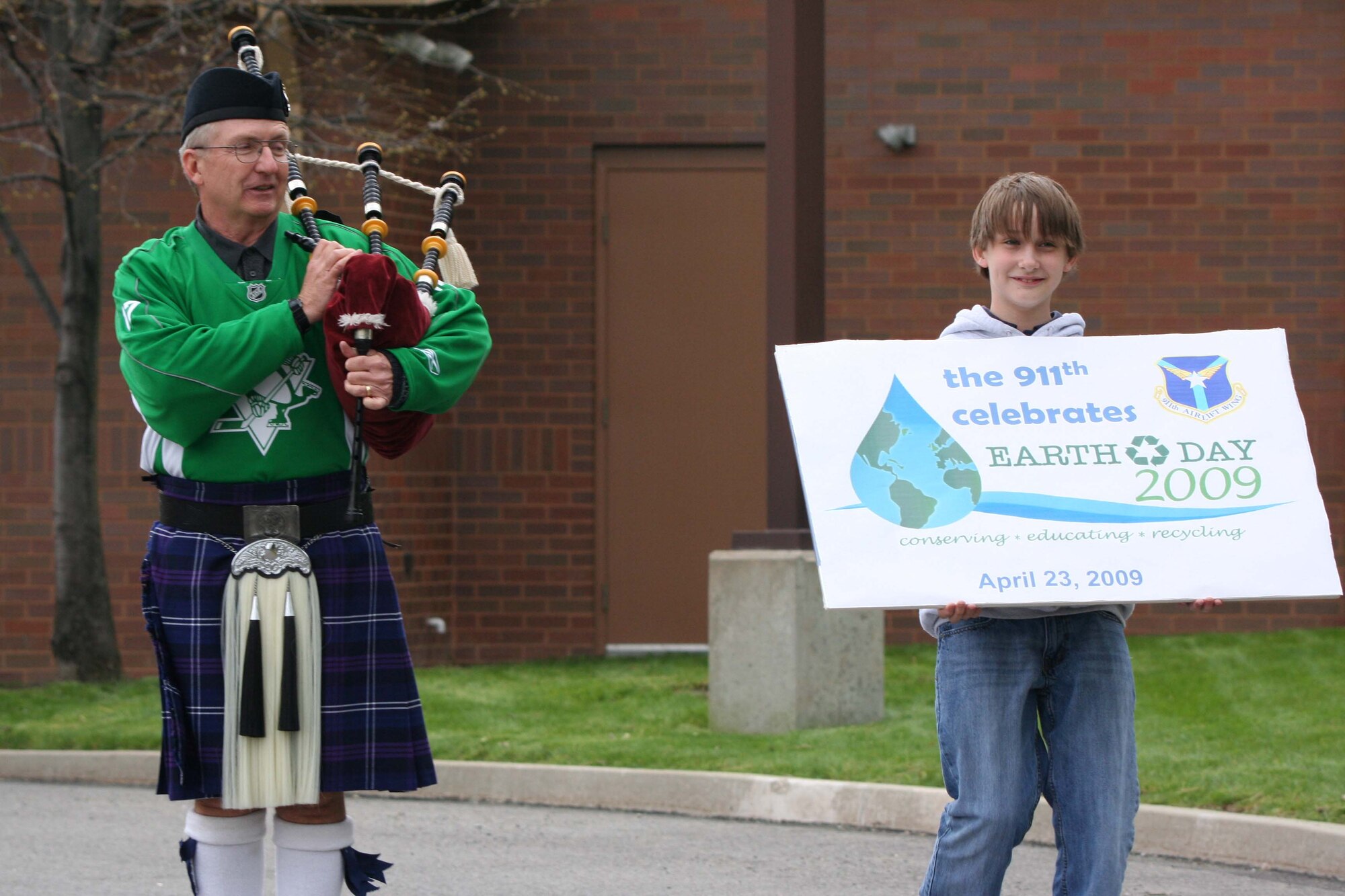 Mr. Robert Clifford, a general engineer with civil engineering, 911th Airlift Wing plays the bagpipes while his son, Robert Patrick Clifford, holds up a banner for the 911th AW Earth Day event. The event was part of the celebration for the 14th Annual Tree Planting Ceremony held here April 23, 2009.(U.S Air Force photo by Staff. Sgt Roberto Modelo.)