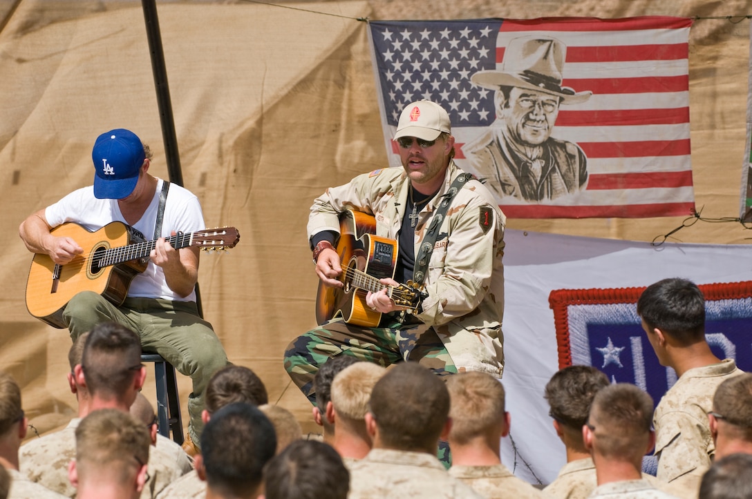 Country music megastar Toby Keith started his seventh USO tour in Afghanistan April 21, 2009, and has been putting on shows at a series of remote forward operating bases, most of which haven't had any outside entertainment come through in six months. Here, Keith entertains Marines at FOB #2 in Bakwa. Looking over his shoulder, graphically depicted on an American flag, is movie legend John Wayne. At left is Scotty Emerick, a fellow performer and regular on the Toby Keith tours. USO photo by Dave Gatley