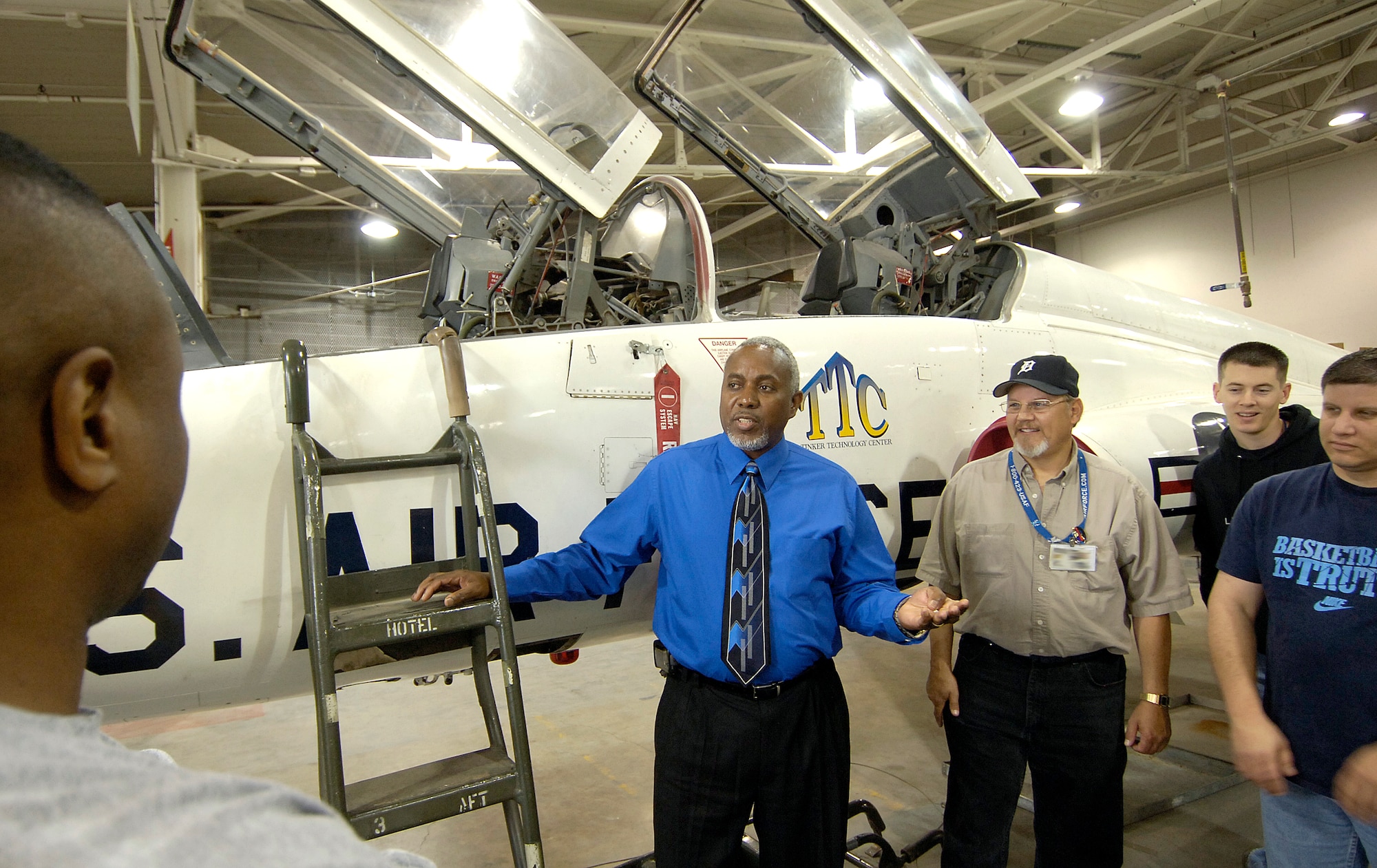Against a T-38 used for training mechanics, Tinker Technology Center Director Jefferson Tarver, center, talks about the aircraft with students.  The center, located in Bldg. 1, houses the jet and other areas where mechanics can learn hands-on and in the classroom.