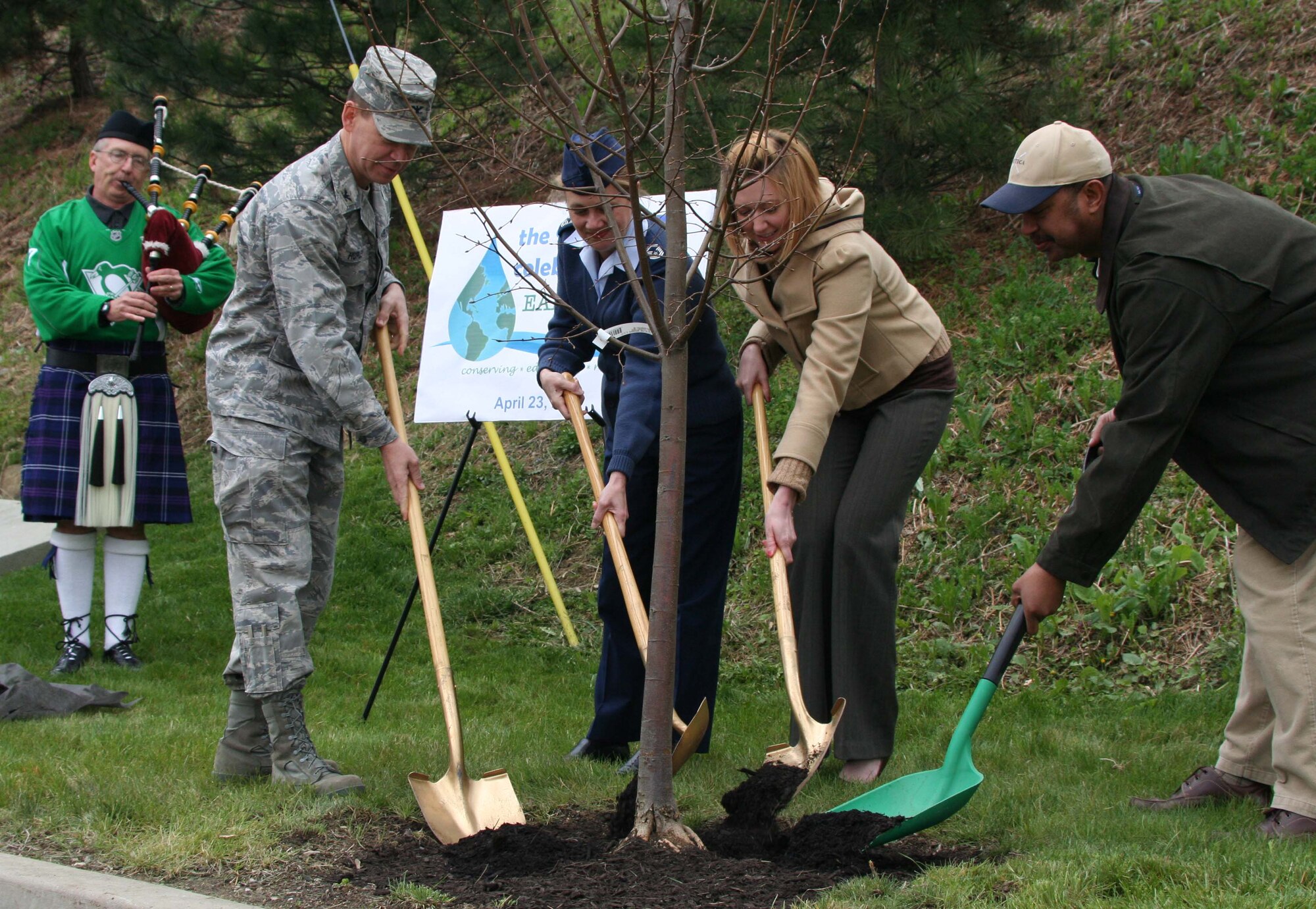 (starting from the left) Col. James Hurley, Commander of the 911th Mission Support Group; Senior Master Sgt. Cari Lennon, Health Services Manager with the 911th Aeromedical Staging Squadron ; Ms. Ashley Pennington, a contracting officer with the 911th Contracting Flight; and Mr. Adrian Mood, a civil engineer with the 911th Civil Engineering Flight put the finishing touches on planting a tree here, April 23, 2009, in recognition of Earth Day. This represented the 14th Annual Tree Planting Ceremony held here.  Mr. Robert Clifford, 911th Civil Engineers, adds some background music with the bagpipes.(photo by Staff. Sgt Roberto Modelo)