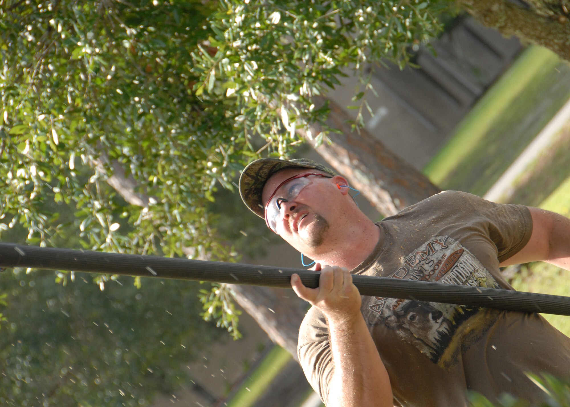 Saw dust rains down as Wesley Flowers, 796th Civil Engineer Squadron, cuts some of the lower branches of a tree along Drone Street Aug. 1 at Duke Field.  (U.S. Air Force photo/Staff Sgt. Samuel King Jr.)