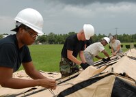Senior Airman Deandrea Dorsey, 919th Services Flight, and others tie down the flaps July 31 while building a tent to be used as a kitchen for a deployment training exercise.   Services members built two tents to be used as a kitchen and dining facility as part of their training.  The building was plagued by frequent thunderstorms that popped up throughout the process.  Personnel prepared and ate a meal from the tents Aug. 1 during the UTA weekend.  (U.S. Air Force photo/Staff Sgt. Samuel King Jr.)