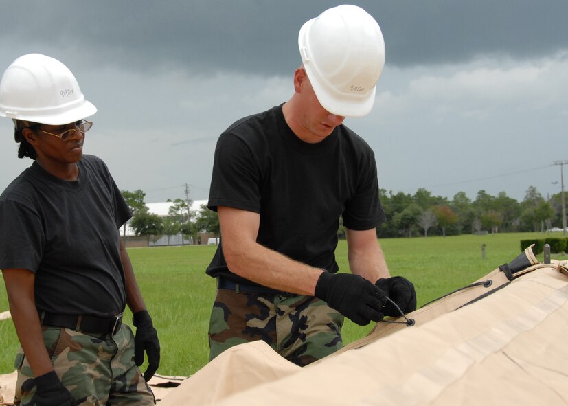 (Right) Tech. Sgt. Wesley Barnett, 919th Services, explains how to secure the ties on the tent flaps to Staff Sgt. Sharon Edwards, 919th Services, July 31 while building a tent to be used as a kitchen for a deployment training exercise.   Services members built two tents to be used as a kitchen and dining facility as part of their training.   The building of the tents was plagued by frequent thunderstorms that popped up throughout the process.  Personnel prepared a meal for the 919th Security Forces Squadron from the tents Aug. 1 during the UTA weekend.   (U.S. Air Force photo/Staff Sgt. Samuel King Jr.)