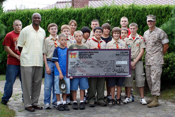 Lt. Col. Jonathan Gackle, Marine Aviation Logistics Squadron 12 commanding officer (right), and Jeffery Fleming, MALS-12 family readiness officer (left), pose for a group picture with Boy Scouts Iwakuni Troop 77 at the Boy Scouts Lodge here Aug. 3. Gackle presented a $100 check on behalf of MALS-12 as a way to support and thank the troop for the help they‘ve given the community and squadron in the past.