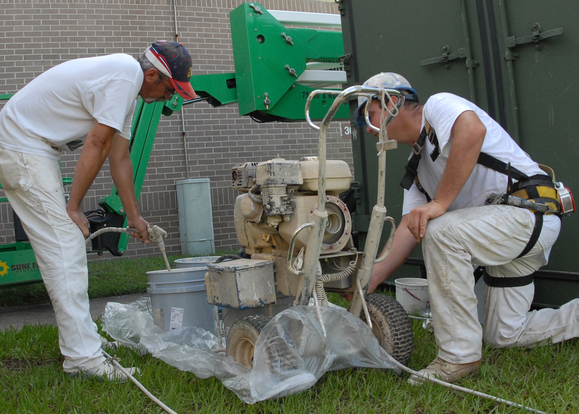 (Left) Mark Stedge and Ray Callin, Washington Painting, work to fill up the paint spray gun before painting the top of the 919th Special Operations Group building Aug. 3 at Duke Field.  The painting crew is moving around repainting many of the base buildings.  (U.S. Air Force photo/Staff Sgt. Samuel King Jr.)