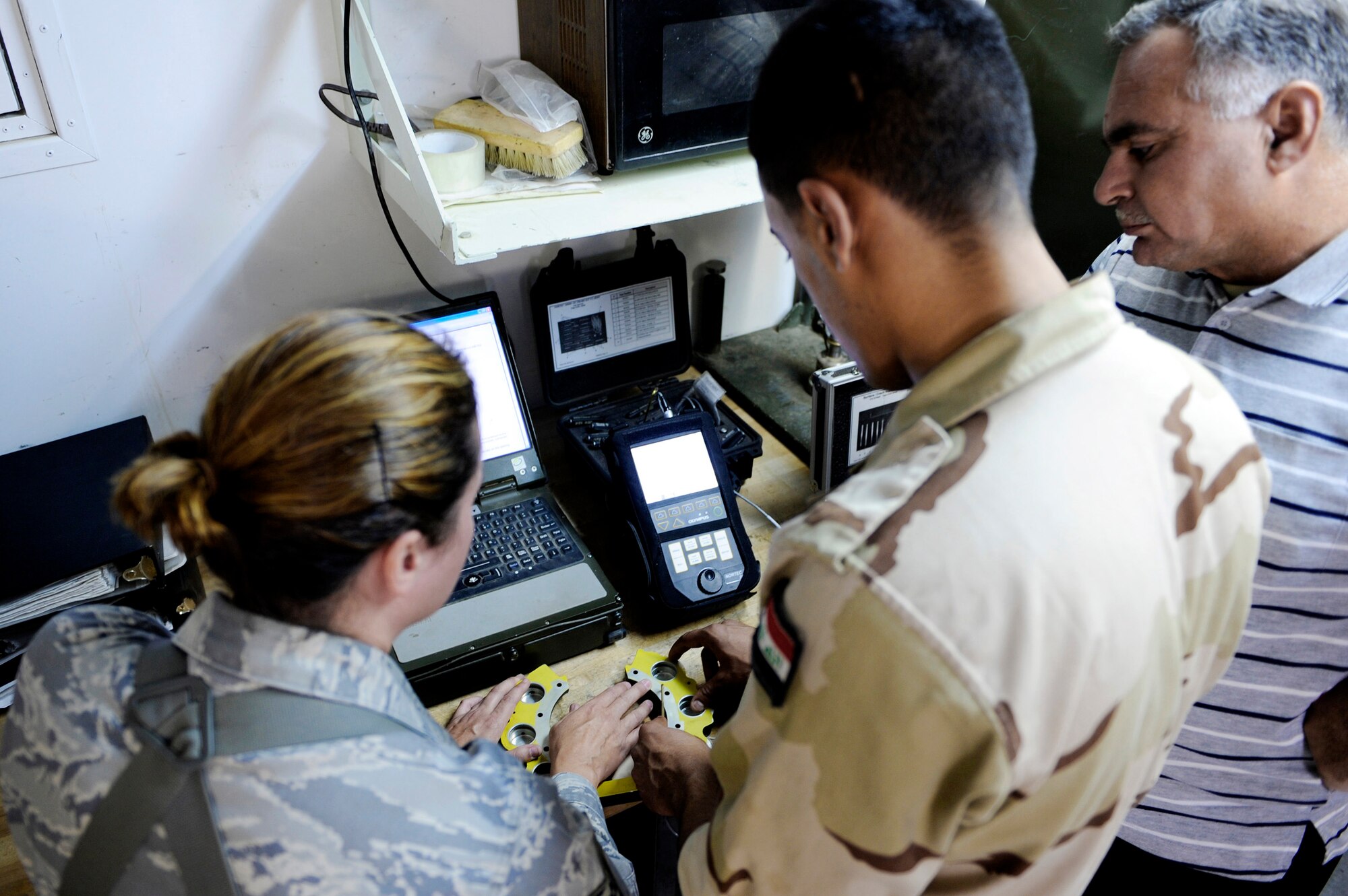 Tech. Sgt. Andrea Walton assists an Iraqi air force maintenance student using specialized tools to find microscopic cracks and flaws in aircraft parts during a training visit to the Army's NDI backshop July 13 at Taji Air Base, Iraq. Sergeant Walton is a nondestructive inspection instructor with the 721st Air Expeditionary Advisory Squadron. (U.S. Air Force photo/Staff Sgt. Michael B. Keller)