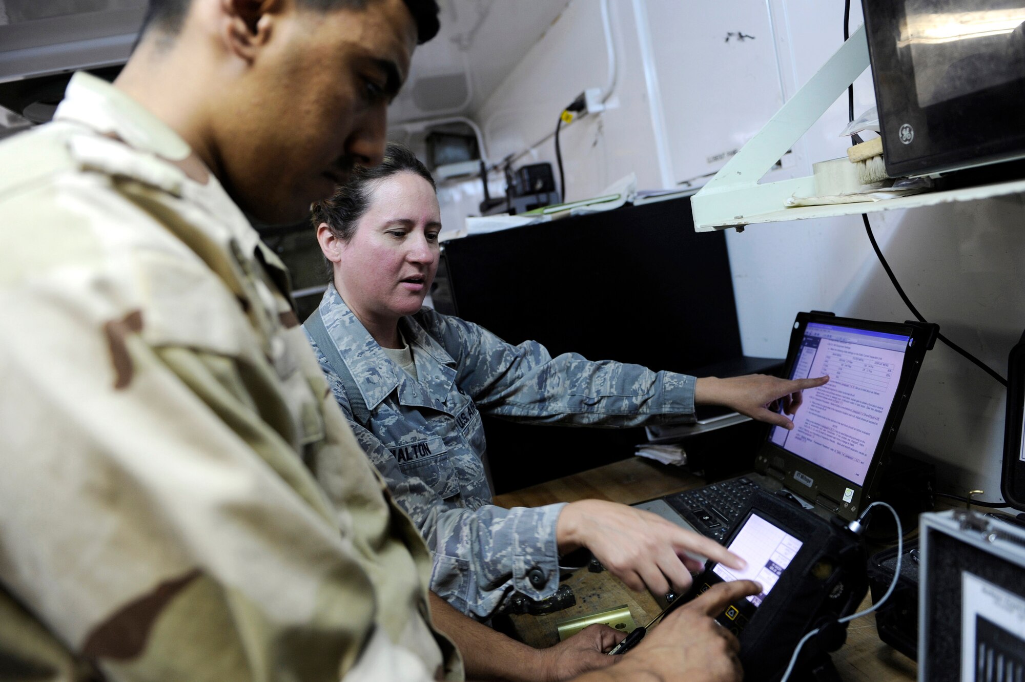 Tech. Sgt. Andrea Walton assists an Iraqi air force maintenance student using specialized tools to find microscopic cracks and flaws in aircraft parts during a training visit to the Army's NDI backshop July 13 at Taji Air Base, Iraq. Sergeant Walton is a nondestructive inspection instructor with the 721st Air Expeditionary Advisory Squadron. (U.S. Air Force photo/Staff Sgt. Michael B. Keller)