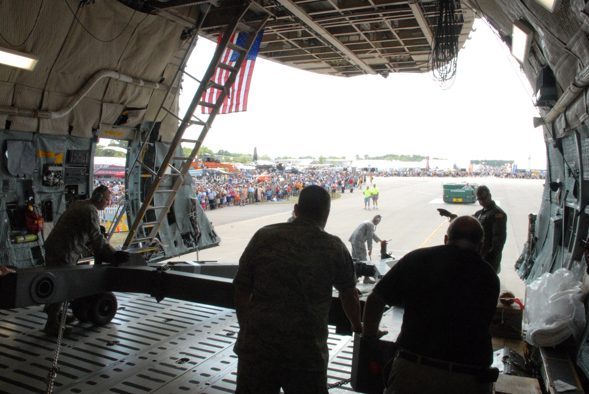 Team Dover members unload aircraft as EAA AirVenture Oshkosh visitors wait for the opportunity to tour the C-5M Super Galaxy.  More than 10,000 guests toured the aircraft during The Spirit of Normandy?s two-day visit to the event.  (U.S. Air Force photo/Staff Sgt. Chad Padgett)