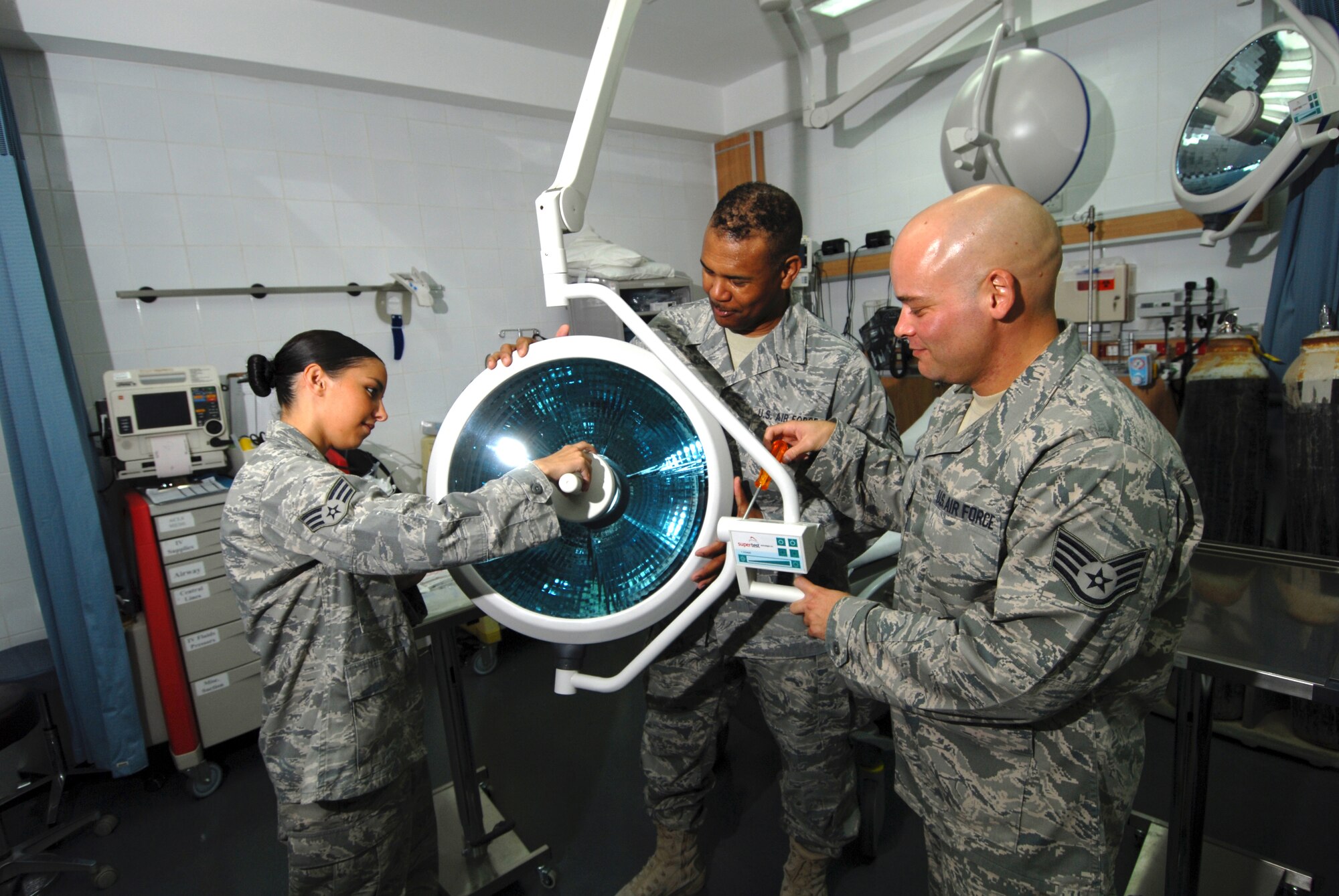 Left to right, Senior Airman Candice Cimball, 379th Expeditionary Medical Group medical logistics technician, Master Sgt. Lancelott Harris, 379 EMDG medical logistics NCOIC, and Staff Sgt. William Travis, 379 EMDG biomedical equipment technician, install new surgical operating lights in the clinic’s emergency room, here, Aug. 5. Airman Cimball hails from Seattle and is deployed from Keesler Air Force Base, Miss. Sergeant Harris is a native of Lauderhill, Fla., and is assigned here as permanent party. Sergeant Travis is a native of Gulf Port, Miss., and deployed from Keesler AFB. All servicemembers are supporting Operations Iraqi and Enduring Freedom.  (U.S. Air Force Photo/Tech. Sgt. Jason W. Edwards)