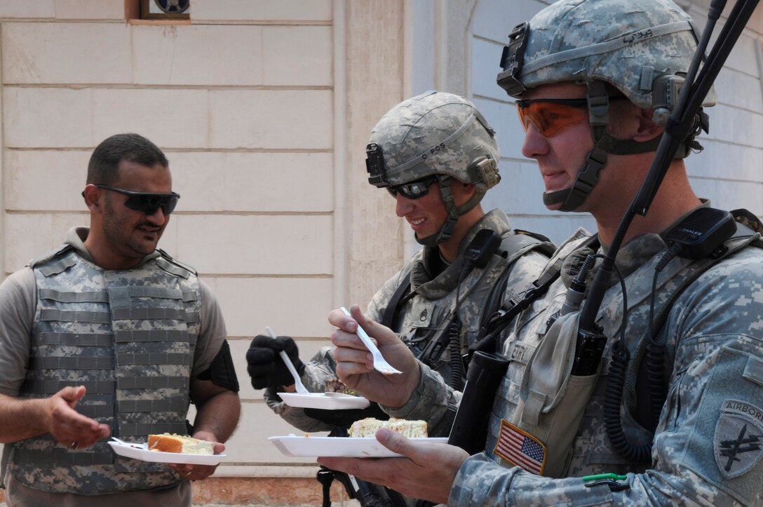 U.S. Army Staff Sgt. James Terry and U.S. Army Staff Sgt. Jason Manella take a break to eat cake with a translator during an assessment of construction progressof the Basra Talent School and the Al Jameat and Al Quibla markets, Basra, Iraq, July 29, 2009.  Both are assigned to the 445th Civil Affairs Battalion's Company B.