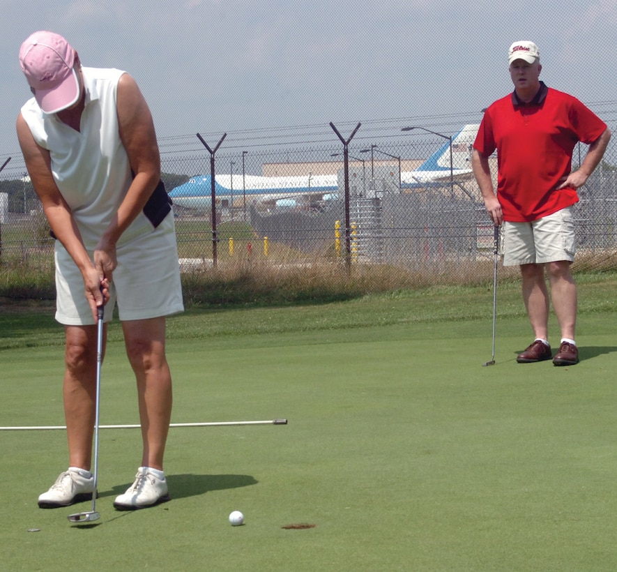 Bonnie Whittington, 316th Force Support Squadron, short putts one in for her team as Richard Cousino, Presidential Airlift Group, observes during an Intramural Golf Tournament playoff game at The Courses at Andrews Tuesday. (U.S. Air Force photo/ Bobby Jones)