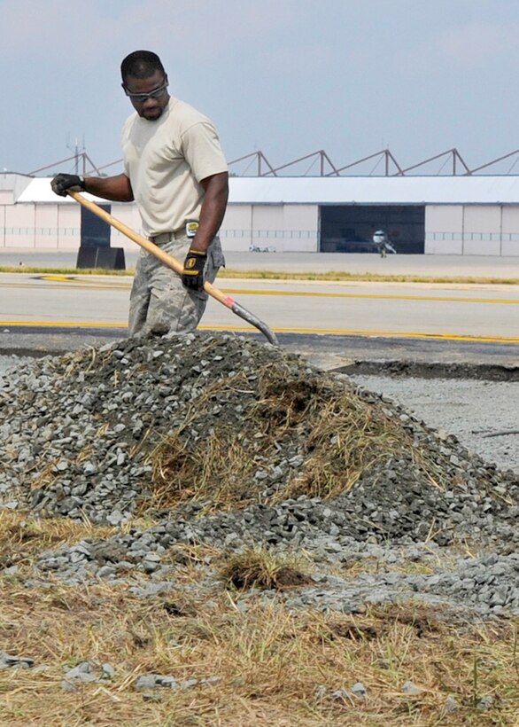 Staff Sgt. Jerime Garvin, 316th Civil Engineer Squadron pavement and constructions craftsman, shovels rocks into a pile for pick up on Andrews flightline July 28. The 316 CE Airmen continuously work on different construction projects in an effort to upgrade the runway and facilities on base. (U.S. Air Force photo/ Senior Airman Giang Nguyen)