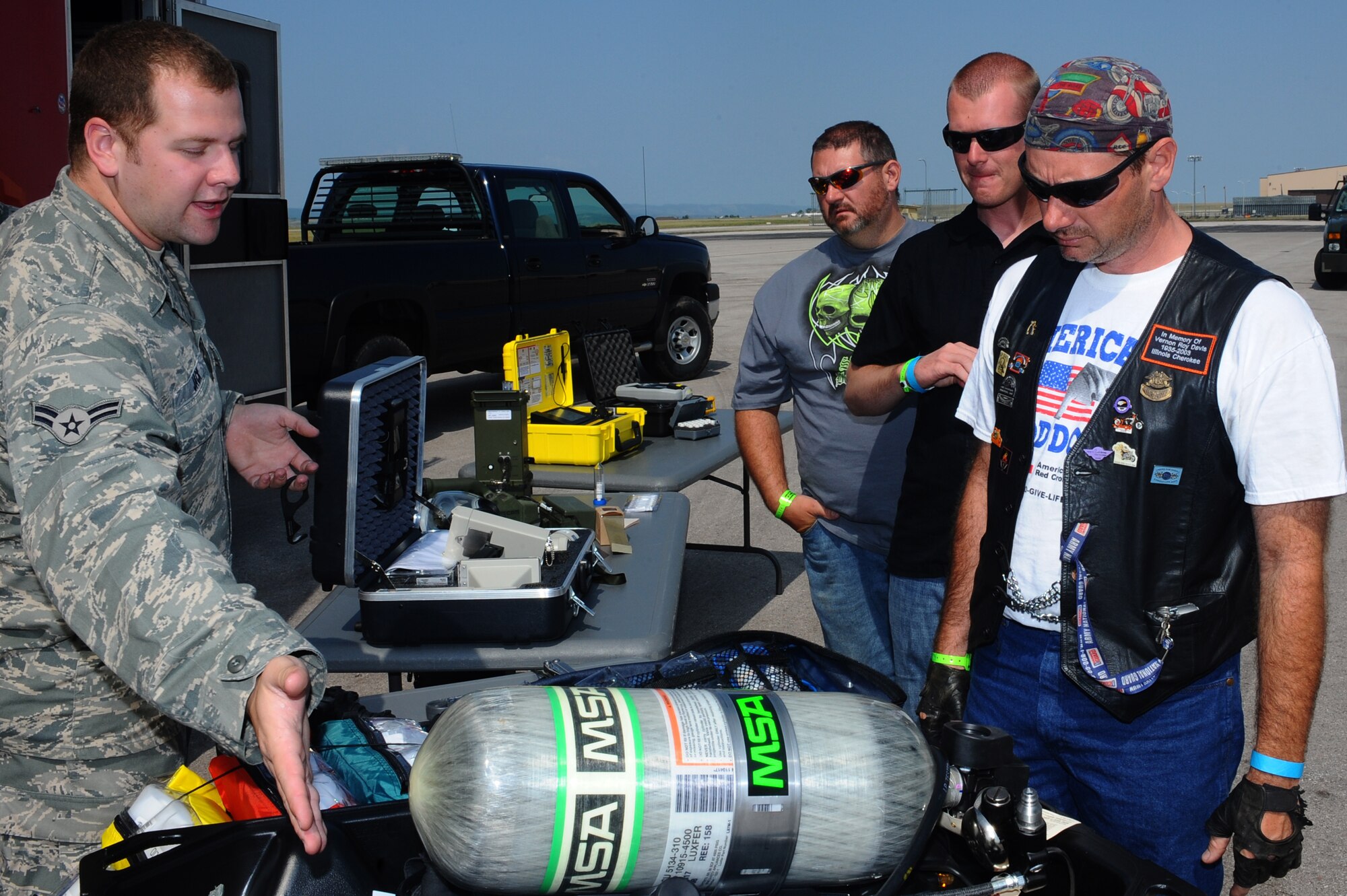Airman 1st Class David Jack (left), 28th Civil Engineer Squadron emergency management technician, explains the purpose of a  Firehawk self-contained breathing apparatus to motorcyclists before the ninth annual Dakota Thunder Motorcycle Run here, August 4. (From right to left) Ron Davis, Josh Oloff, and Roy Davis. (U.S. Air Force photo/Senior Airman Kasey Zickmund)