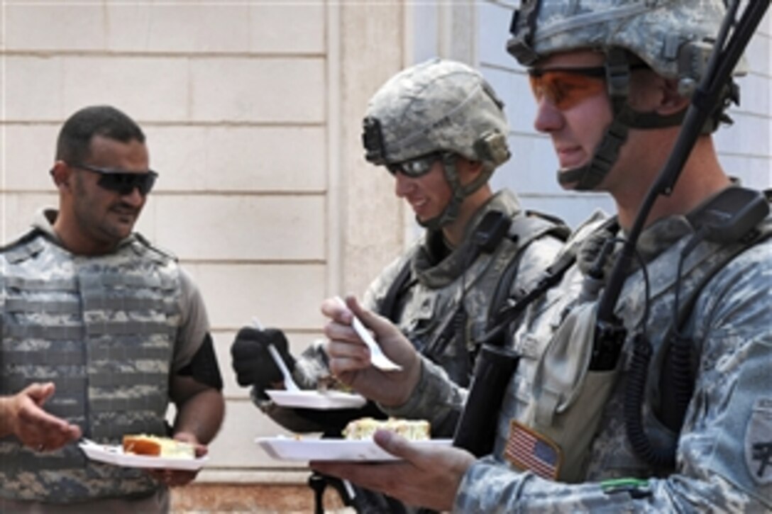 U.S. Army Staff Sgt. James Terry and U.S. Army Staff Sgt. Jason Manella take a break to eat cake with a translator during an assessment of construction progress of the Basra Talent School and the Al Jameat and Al Quibla markets, Basra, Iraq, July 29, 2009.  Both are assigned to the 445th Civil Affairs Battalion's Company B.