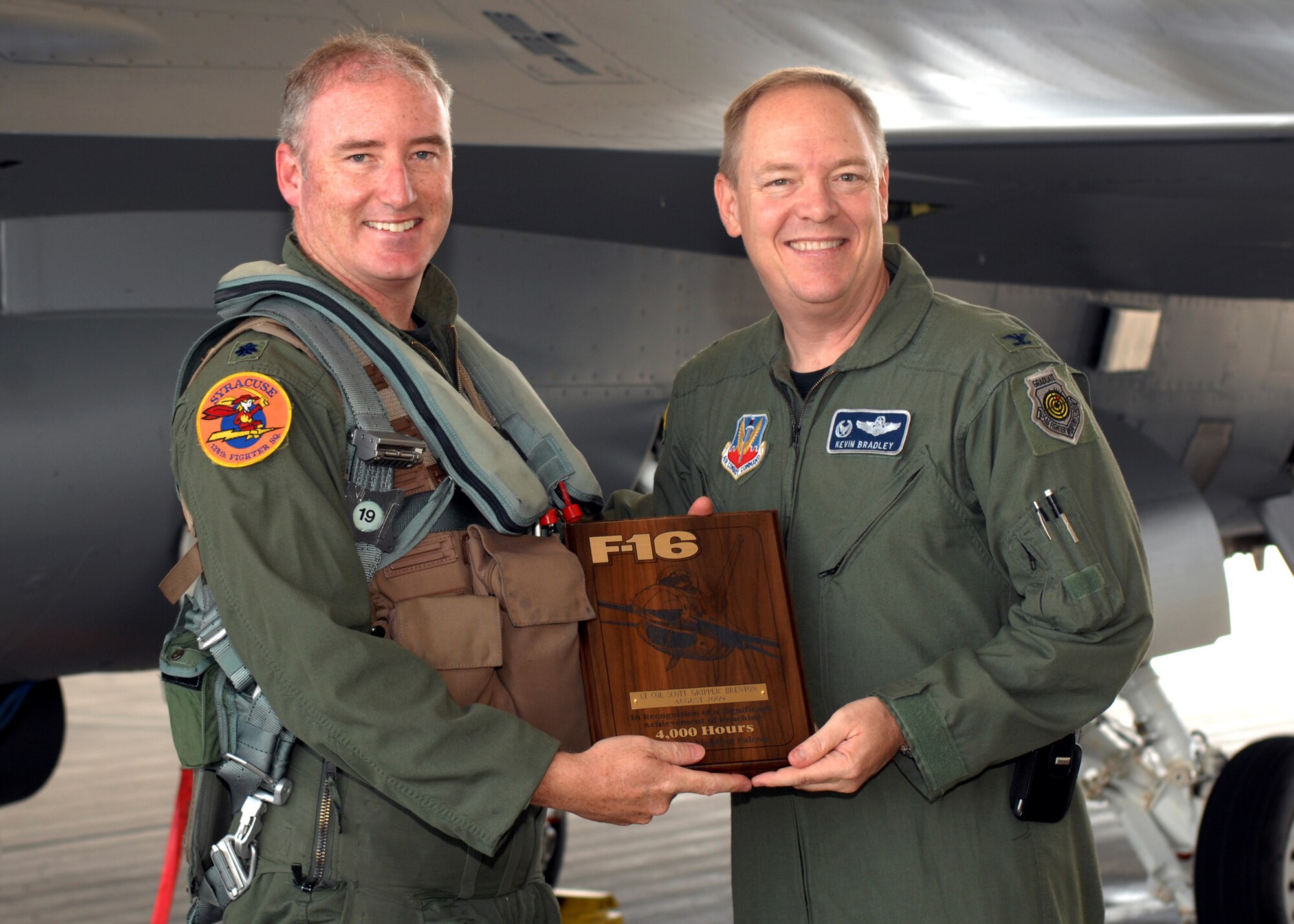 Col. Kevin W. Bradley, 174th Fighter Wing Commander, Syracuse, NY, presents a plaque to Lt. Col. D. Scott Brenton commemorating his achievement of flying more then 4,000 hours inside the cockpit of the F-16 Fighting Falcon.