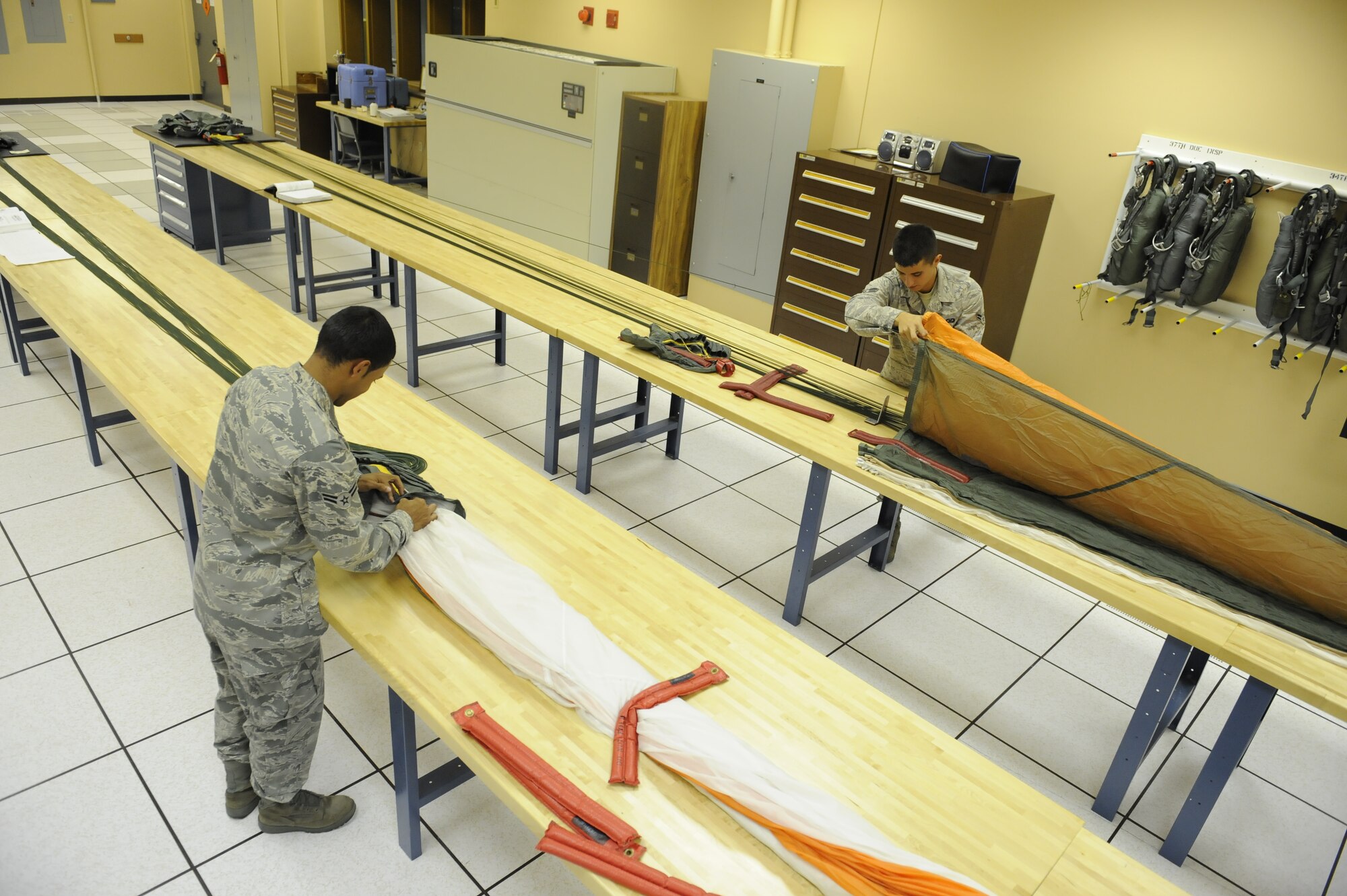 (Left) Airmen 1st Class Devin Hewitt and Stephen Barker, 28th Operations Support Squadron aircrew flight equipment apprentices, inspect and pack several back automatic-22 parachutes here, August 10. The parachutes are inspected and repacked every 180 days. (U.S. Air Force photo by Airman 1st Class Corey Hook)
