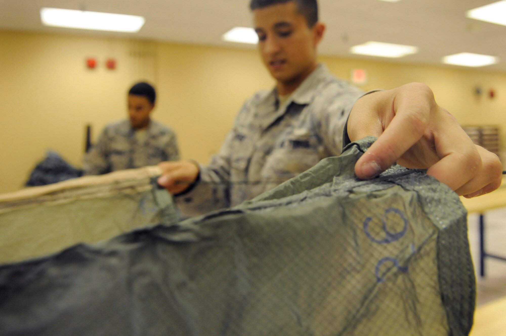 (Left) Airmen 1st Class Devin Hewitt and Stephen Barker, 28th Operations Support Squadron aircrew flight equipment apprentices, inspect and pack several back automatic-22 parachutes here, August 10. The parachutes are inspected and repacked every 180 days. (U.S. Air Force photo by Airman 1st Class Corey Hook)