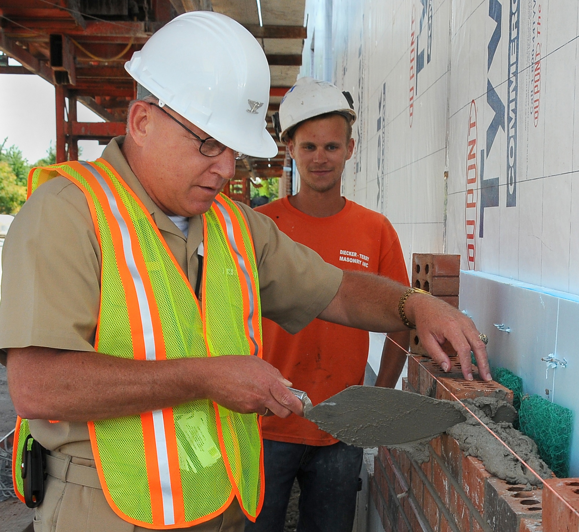 SCOTT AIR FORCE BASE, Ill. -- Navy Capt. Michael Murray, U.S. Transportation Command Intelligence Director,  makes a contribution to the brick side of the new Joint Intelligence Operations Center at Scott while Matt Baker, brick foreman for Dieker Terry Masonry Inc., supervises.  The facility will provide 28,000 square-feet to be occupied by intelligence analysts from USTRANSCOM and the Defense Intelligence Agency. The facility is expected to be completed July 2010.(Photo courtesy Bob Fehringer)