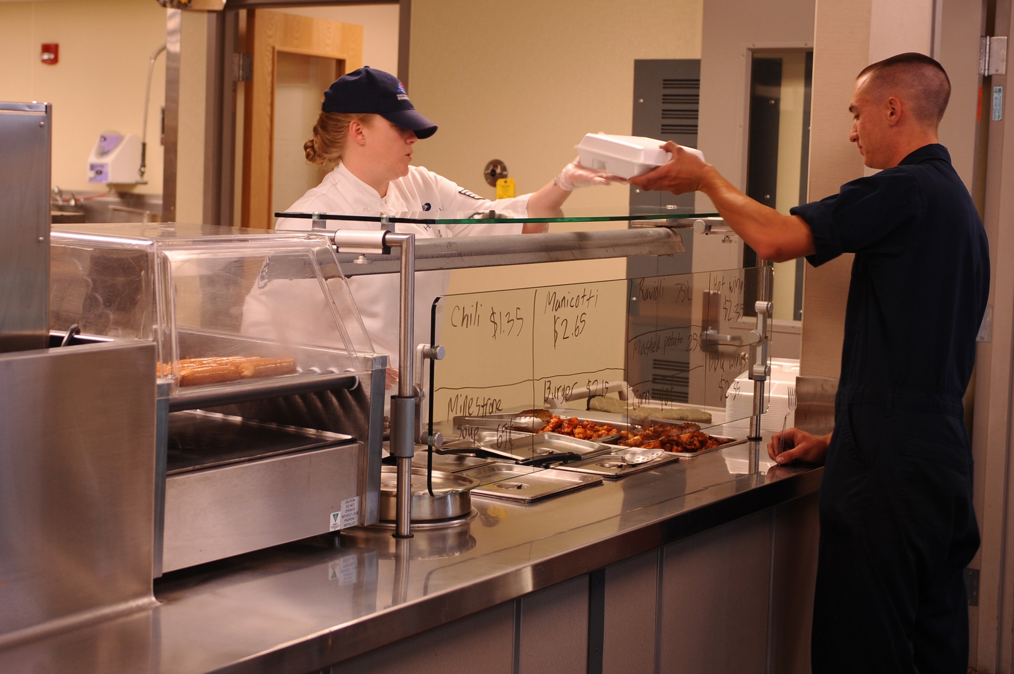 Staff Sgt. Bree-ann Hermosillo, 28th Force Support Squadron assistant flight kitchen manager, hands Senior Airman Brian Decker, 28th Aircraft Maintenance Squadron B-1B Lancer crew chief, his lunch at the flight kitchen here, August 11. The flight kitchen operates 24 hours a day, providing hot meals and pre-made supplement bags containing various food items. (U.S. Air Force photo/Senior Airman Kasey Zickmund)