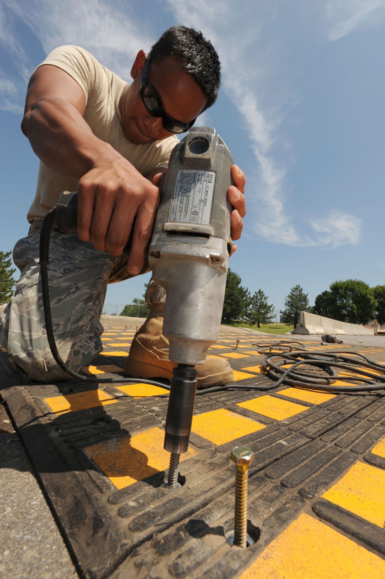 WHITEMAN AIR FORCE BASE, Mo. – Airman 1st Class Ralph Dagza, 509th Civil Engineer Squadron, uses an impact drill to run bolts into speed humps near Arnold Gate, Aug. 11. Each individual piece of the speed humps must be laid out and predrilled, then bolted down. Arnold gate is receiving three of these new fixtures to be completed by Aug. 12. The Lemay and Spirit gates will also be receiving these fixtures in the upcoming weeks. (U.S. Air Force Photo/Airman First Class Carlin Leslie)