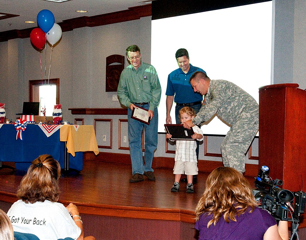 U.S. Army Col. Mark Stammer, commander of the 82nd Airborne Division's 1st Brigade Combat Team, enlists a young spectator to help present Dan Shannon of Operation Homelink and Troy West of Dell Computer with plaques of appreciation for donating computers that will enable families to communicate with their deployed soldiers, Fort Bragg, N.C., Aug. 7, 2009.