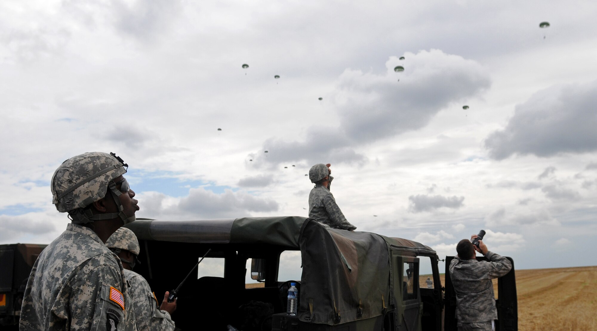 U.S. Army soldiers and Air Force airmen watch as a C-130 Hercules drops over 40 personnel over Bunker drop zone in southwestern, Germany on Aug. 13, 2009. U.S. soldiers and airmen performed a combined airborne jump with four other NATO countries. German, Italian, Belgium, and Dutch army attended the airborne jump during NATO Jump Week. (U.S. Air Force photo by Airman 1st Class Grovert Fuentes-Contreras)