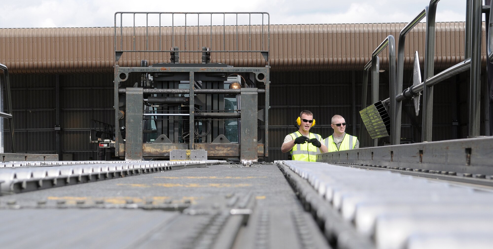 RAF MILDENHALL, England -- Senior Airman Timothy Moore (left) and Airman 1st Class Jason Ivy, both 100th Logistics Readiness Squadron Airmen, fit the forks of a 5-ton forklift to the width of a 25K loader Aug. 13 in the cargo yard. The 25K loader was fit with three pallets before carrying the cargo to an awaiting aircraft. The loader can lift and transport three pallets up to a maximum cargo weight of 25,000 pounds. (U.S. Air Force photo by Senior Airman Thomas Trower)