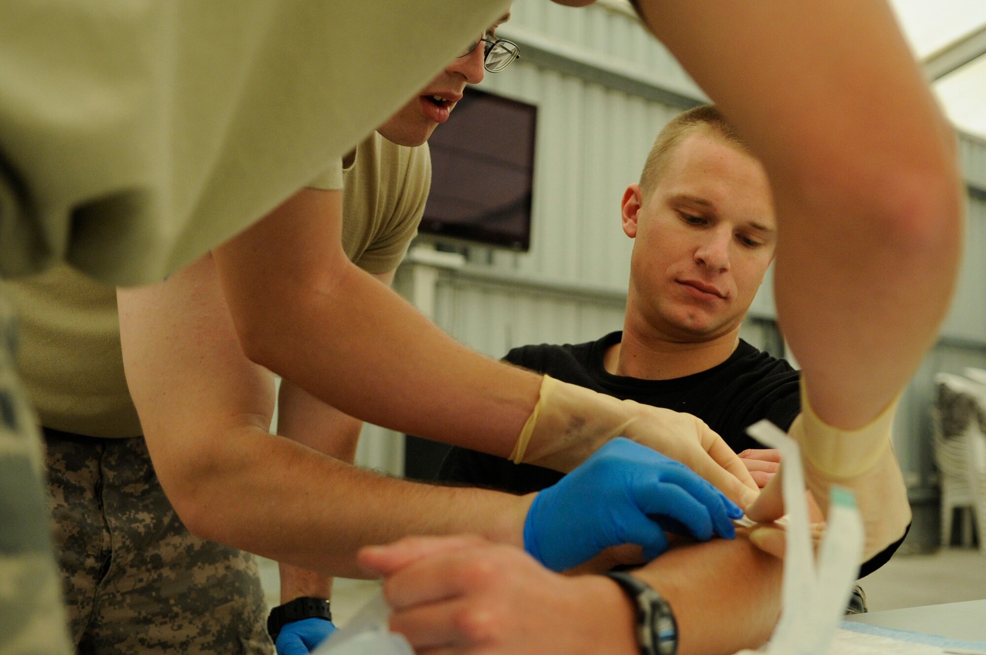 SOUTHWEST ASIA – Staff Sgt. Joshua Hartwell, 380th Expeditionary Civil Engineer Squadron, initiates a saline lock and intravenous infusion on Senior Airman Kyle Dobler, 380th ECES, as Specialist Bryan Haney, a U.S. Army medic, supervises during a Combat Lifesaver Course Aug. 13. The course covers areas such as performing tactical combat casualty care, opening and managing an airway, treating penetrating chest trauma and decompressing a tension pneumothorax, initiating a saline lock and intravenous infusion, and requesting medical evacuation. Sergeant Hartwell is deployed from McConnell AFB, Kan., and hails from Warner Robins, Ga. Airman Dobler is deployed from Peterson AFB, Colo., and hails from Vacaville, Calif. Specialist Haney is deployed from Fort Bliss, Texas and hails from Charlton, Mass. (U.S. Air Force photo/Senior Airman Stephen Linch)