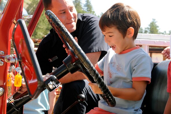Two-year-old Sebastian Smits plays with the steering wheel of a fire truck under the supervision of firefighter Shaun Glidden from Fort Carson, Colo., during a U.S. Air Force Academy Fire Department Open House held Aug. 8. (U.S. Air Force photo/J. Rachel Spencer)