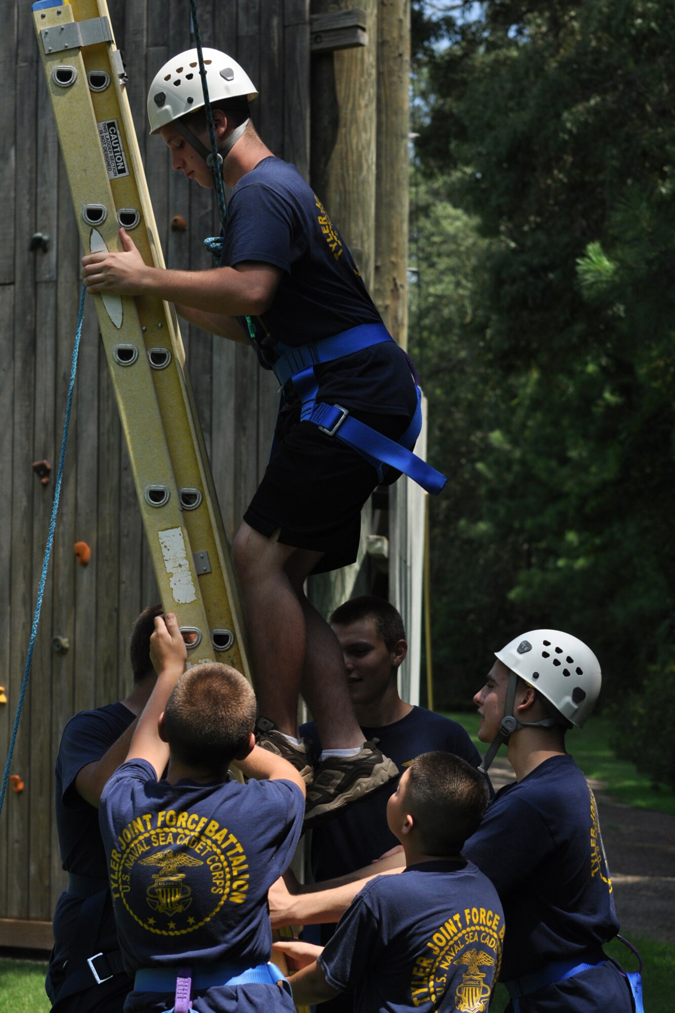 Petty Officer Third Class Patrick Bailey climbs a ladder to walk across a pole hanging some twenty feet in the air as his fellow cadets (spotters) secure the ladder and urge him on to success at the East Texas Medical Center/Behavioral Health Center in Tyler, Texas, August 15, 2009. Petty Officer Bailey is a member of the TYLER JOINT FORCE Battalion of the U.S. Naval Sea Cadets Corps based in Tyler. The exercise helps participants overcome their fears, build confidence in their personal abilities and trust in the support of others. The cadets spent the entire day completing exercises which will enable them to work closer with and trust their fellow cadets and officers. Petty Officer Bailey is from Tyler, Texas. These exercises will also benefit those cadets who decide to join the U.S. Military in the future. (Courtesy photo)  