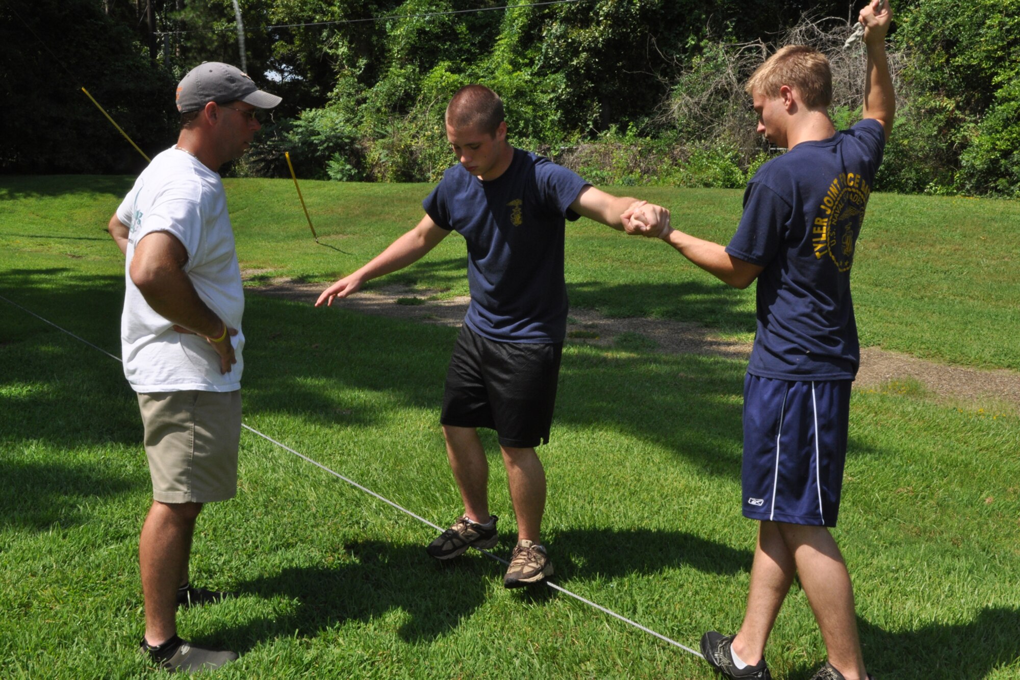 James Whitaker, activities therapy coordinator, East Texas Medical Center/Behavioral Health Center observes cadets from the TYLER JOINT FORCE Battalion of the U.S. Naval Sea Cadets Corps take part in an exercise called “Low Multivine” at the Behavioral Health Center in Tyler, Texas, August 15, 2009. Petty Officer First Class Sam Fiser holds on to a rope and supports Petty Officer Third Class Patrick Bailey as he moves farther down the course and closer to the objective. The exercise is used to enhance team work and trust between the cadets. The exercise also teaches participants the importance of a support system to accomplish their goals. The cadets spent the entire summer day completing exercises which will enable them to work closer with and trust their fellow cadets. Petty Officer Fiser is from Flint, Texas, and Petty Officer Bailey is from Tyler, Texas. This experience will also benefit those cadets who decide to join the U.S. Military in the future. (Courtesy photo) 