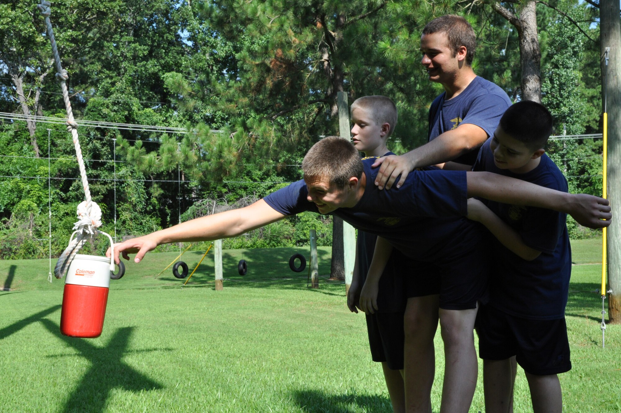 Seaman Apprentice Seth Loftin of the TYLER JOINT FORCE Battalion of the U.S. Naval Sea Cadets Corps slowly pulls in a jug of water as his teammates try to keep him from falling off a platform. The cadets are taking part in an exercise called “Nitro Crossing” at the East Texas Medical Center/Behavioral Health Center in Tyler, Texas, August 15, 2009. The exercise, which involves swinging on a rope across an expanse to their teammates who are standing on a two foot by two foot platform, is used to enhance the planning process and trust between the cadets. The exercise also requires the cadets, at some point during the exercise, to get the jug of water across the expanse to their teammates without spilling a drop. The exercise, which proved to be very difficult to accomplish, will also benefit those cadets who decide to join the U.S. Military in the future. Seaman Loftin’s hometown is Tyler, Texas. (Courtesy photo)      