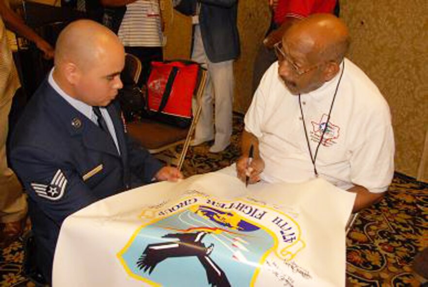 Staff Sgt. Manny Acuna, 477th Fighter Group Maintenance Squadron, holds a banner for Lt. Col. Alvin Spann to sign on a symbolic group patch at the Tuskegee Airmen's 38th Annual National Convention held in Las Vegas, Nev.  Several members of the 477th Fighter Group attended the convention to meet and honor the courageous aviators from World War II, that not only fought the Nazis overseas but battled discrimination at home.  The 477th FG's history traces back to the original Tuskegee Airmen as its 302nd Fighter Squadron was part of the 332nd Fighter Group, also known as the famed 'Redtails.'  The 477th is connected to another Tuskegee Airmen unit--the 477th Bombardment Group-- that was activated in 1944.  The 477th BG members trained and were ready to deploy just as the war ended.   Several other original Tuskegee Airmen attended the 2007 reactivation ceremony of the 477th Fighter Group, linking their incredible heroism and courage during WWII with the 477th FG's exciting future. (Air Force Photo / Maj. Cary McPartlin)