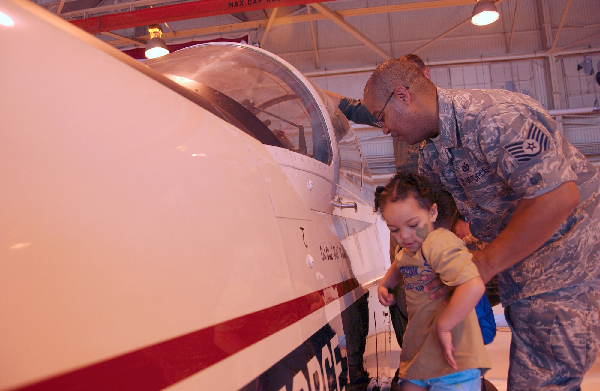 Technical Sgt. Antonio Smith lifts his daughter up to see the T-6A Texan II at Camp Liberty in Hangar 170, the “deployment” site for the Operation KIDS participants, Aug. 6 at Vance AFB, Okla. The event was a hands-on activity for children of military families to learn about their parents’ deployment process.  (U.S. Air Force photo/ 1st Lt. Agneta Murnan)