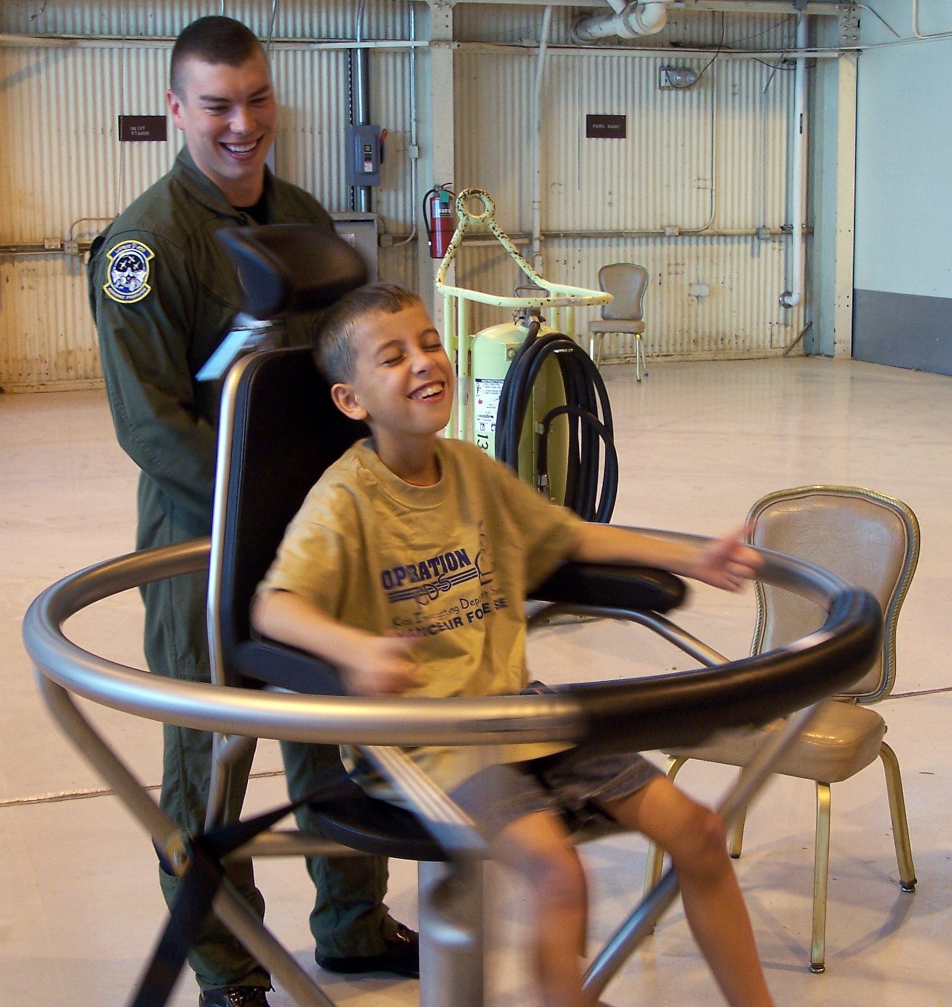 Senior Airman Joseph Santiago spins Matthew Hofler, participant of the Operation KIDS event, Aug. 6 at Vance AFB, Okla., in the spin chair at the “deployment” site, Camp Liberty, located in Hangar 170. The event was a hands-on activity for children of military families to learn about their parents’ deployment process. (U.S. Air Force photo/ Lisa Hoth)