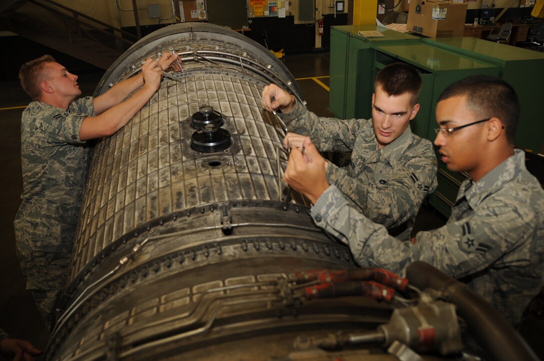 (Left to right) Airman 1st Class Jason Pettine, Justin Hildreth and Khayan Martinez, 28th Maintenance Squadron aerospace propulsion apprentices, remove bolts from a fan duct on a B-1B Lancer engine here, August 13.  The Airmen remove the fan duct to access blades in need of repair. (U.S. Air Force photo/Airman 1st Class Anthony Sanchelli)