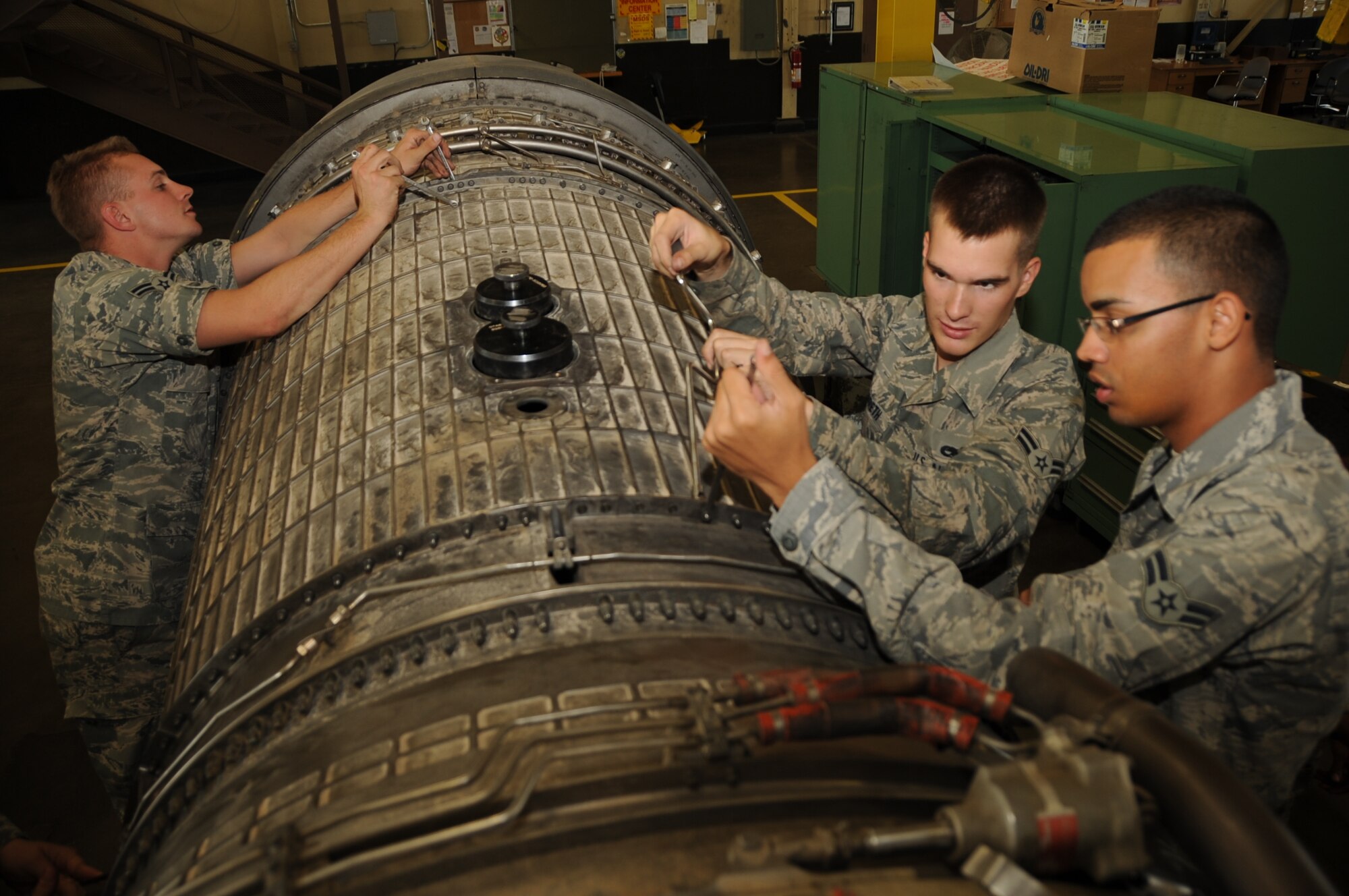 (Left to right) Airman 1st Class Jason Pettine, Justin Hildreth and Khayan Martinez, 28th Maintenance Squadron aerospace propulsion apprentices, remove bolts from a fan duct on a B-1B Lancer engine here, August 13.  The Airmen remove the fan duct to access blades in need of repair. (U.S. Air Force photo/Airman 1st Class Anthony Sanchelli)
